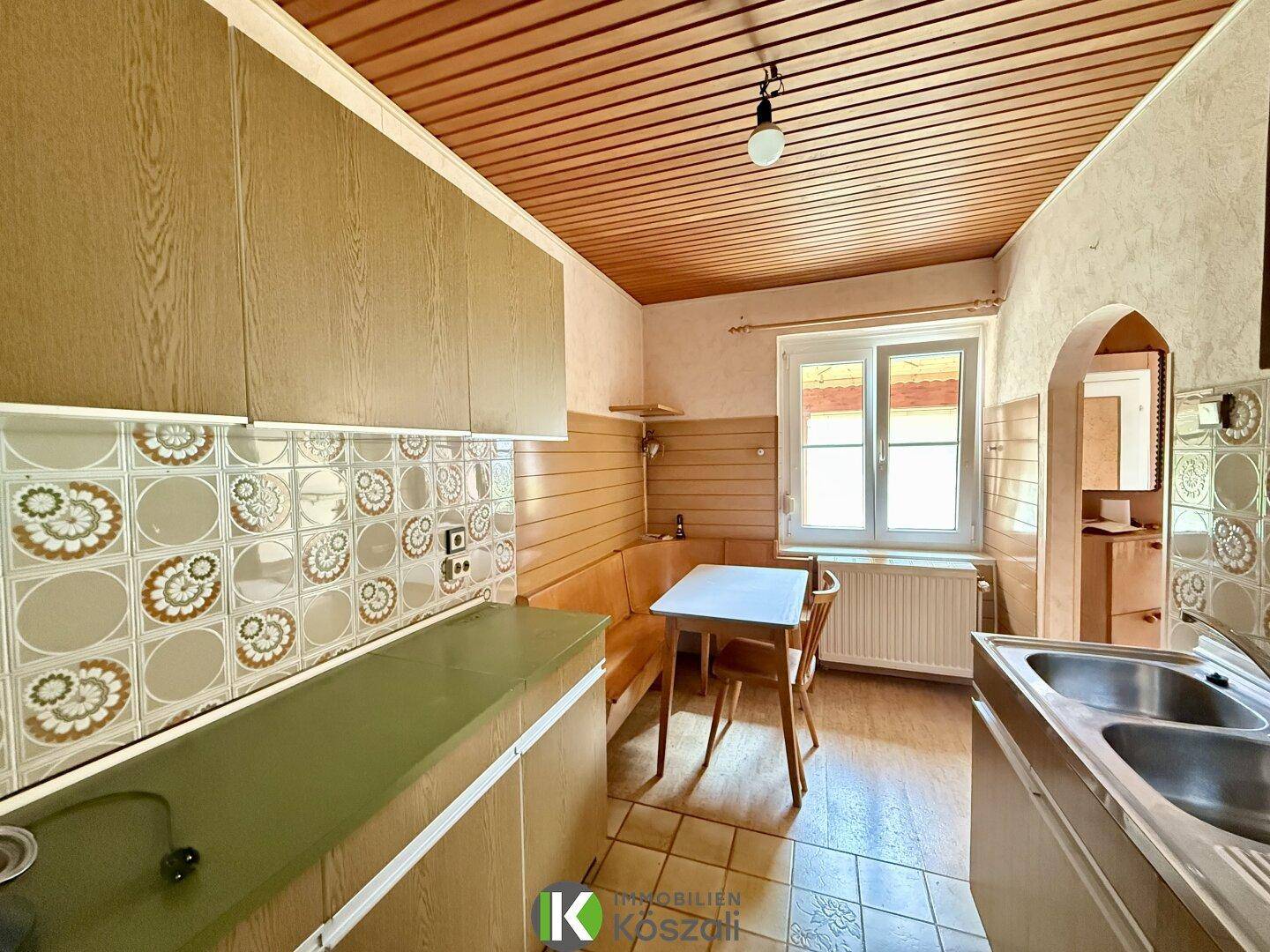Gemütliche Küche mit Holzschränken, Fliesenboden und Spülbecken, ideal für Mahlzeiten.