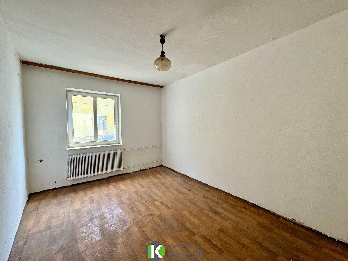 Schlafzimmer mit altem Parkettboden und Heizkörper unter dem Fenster, benötigt Renovierung.