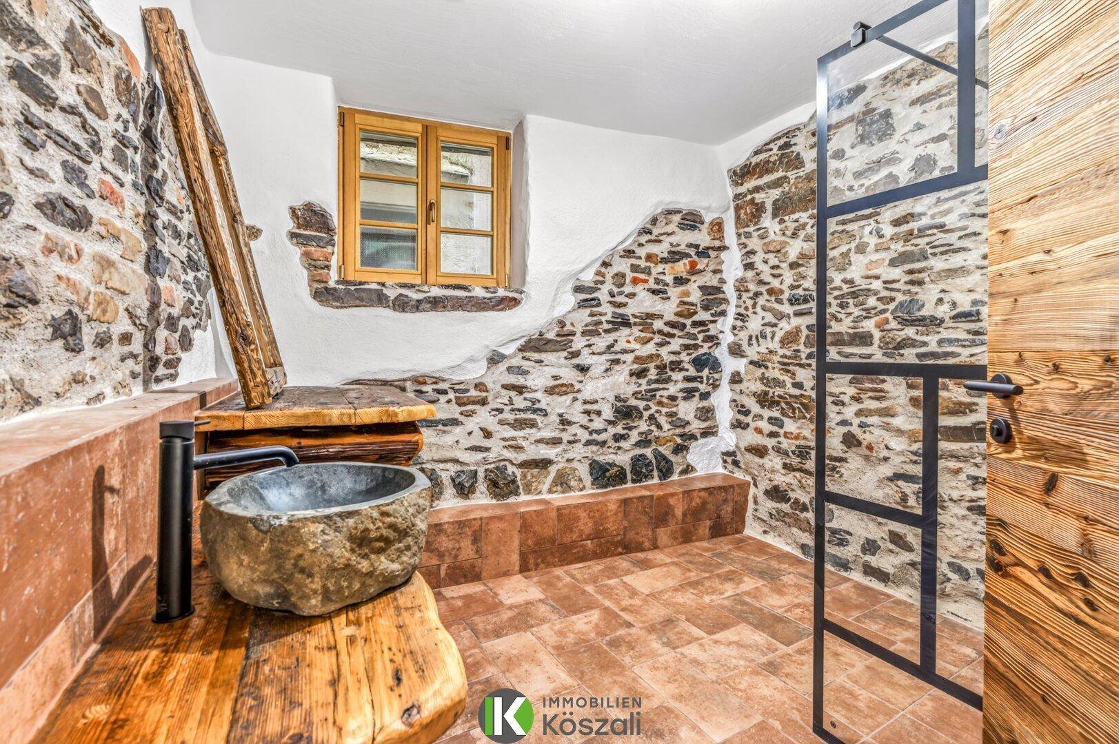Rustikales Badezimmer mit Steinwaschbecken, begehbarer Dusche und freigelegten Steinwänden.