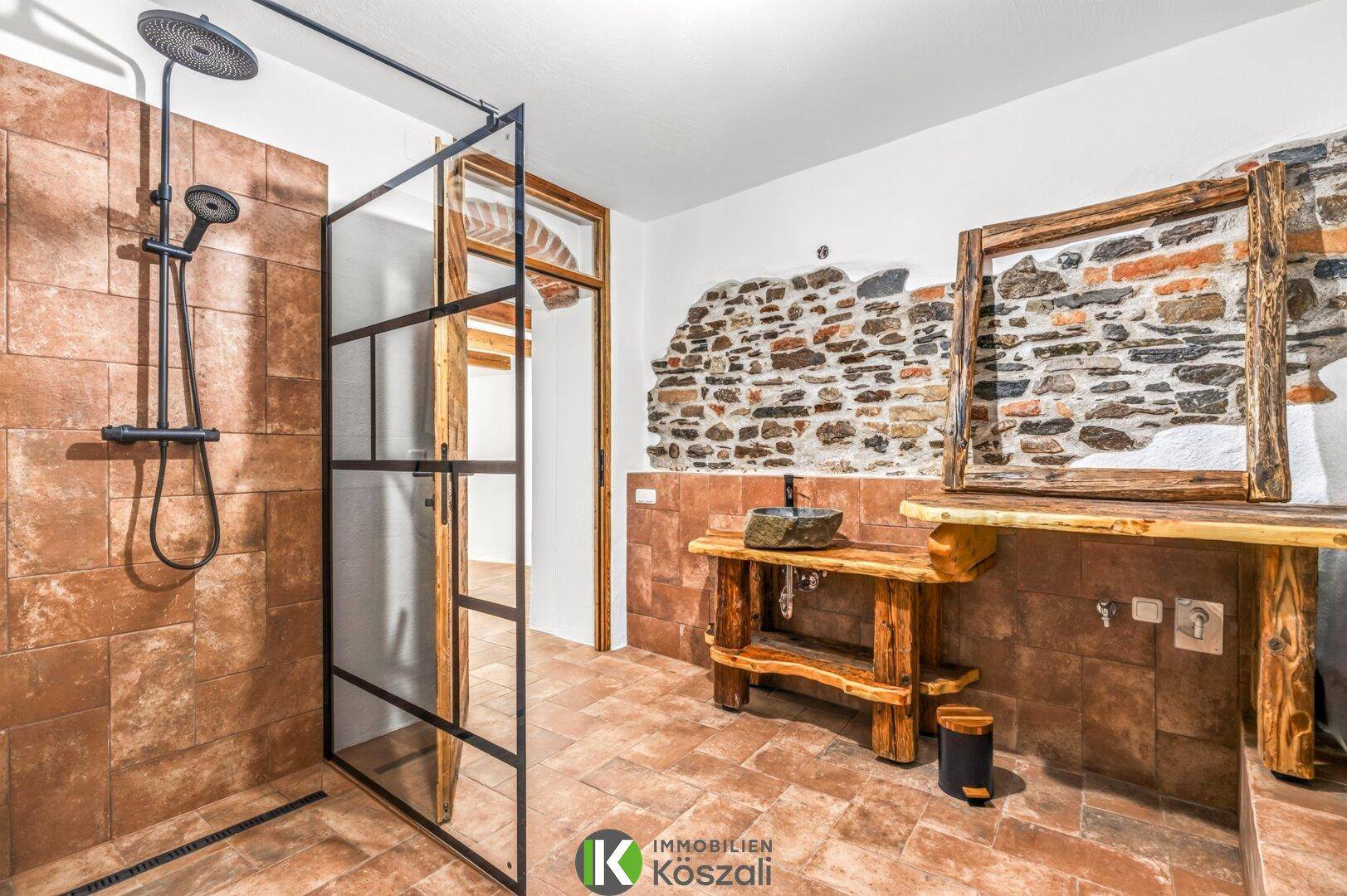 Geräumiges Badezimmer mit begehbarer Dusche, Steinwaschbecken und rustikalen Holzelementen.