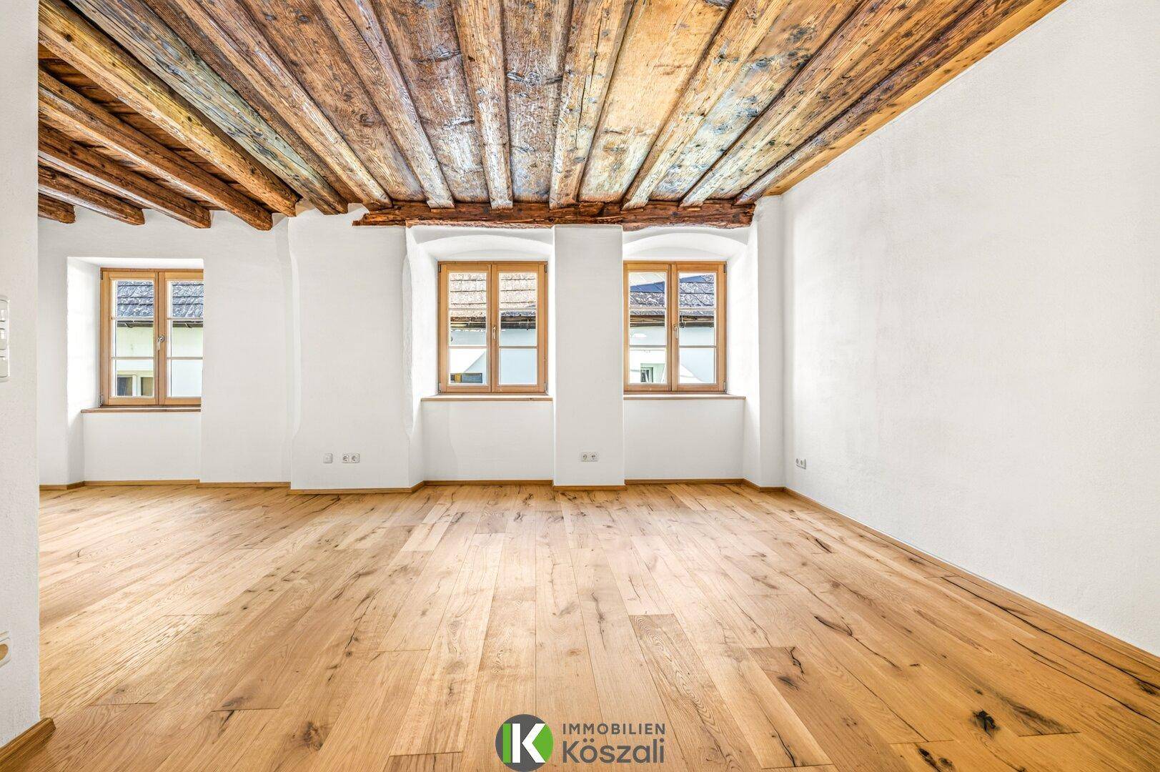 Geräumiges Wohnzimmer mit Holzbalkendecke, Eichenparkett und mehreren Fenstern für viel Licht.