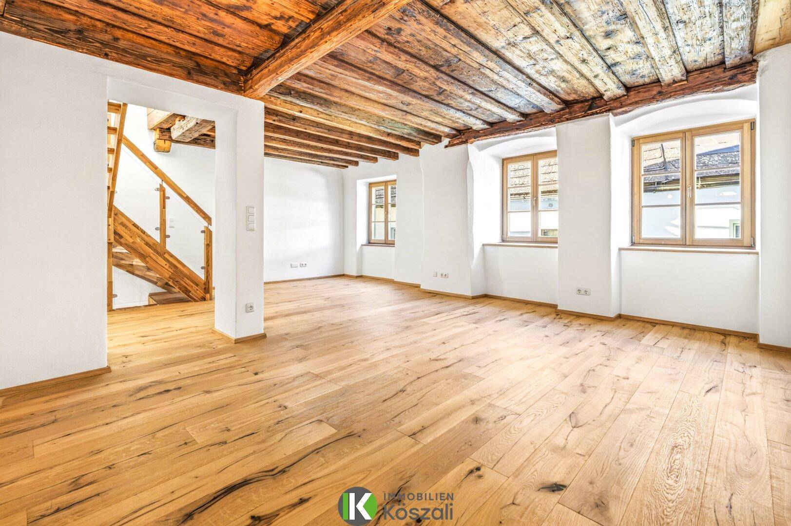 Helles Wohnzimmer mit Eichenparkett, Holzbalkendecke und Zugang zu einer Holztreppe.