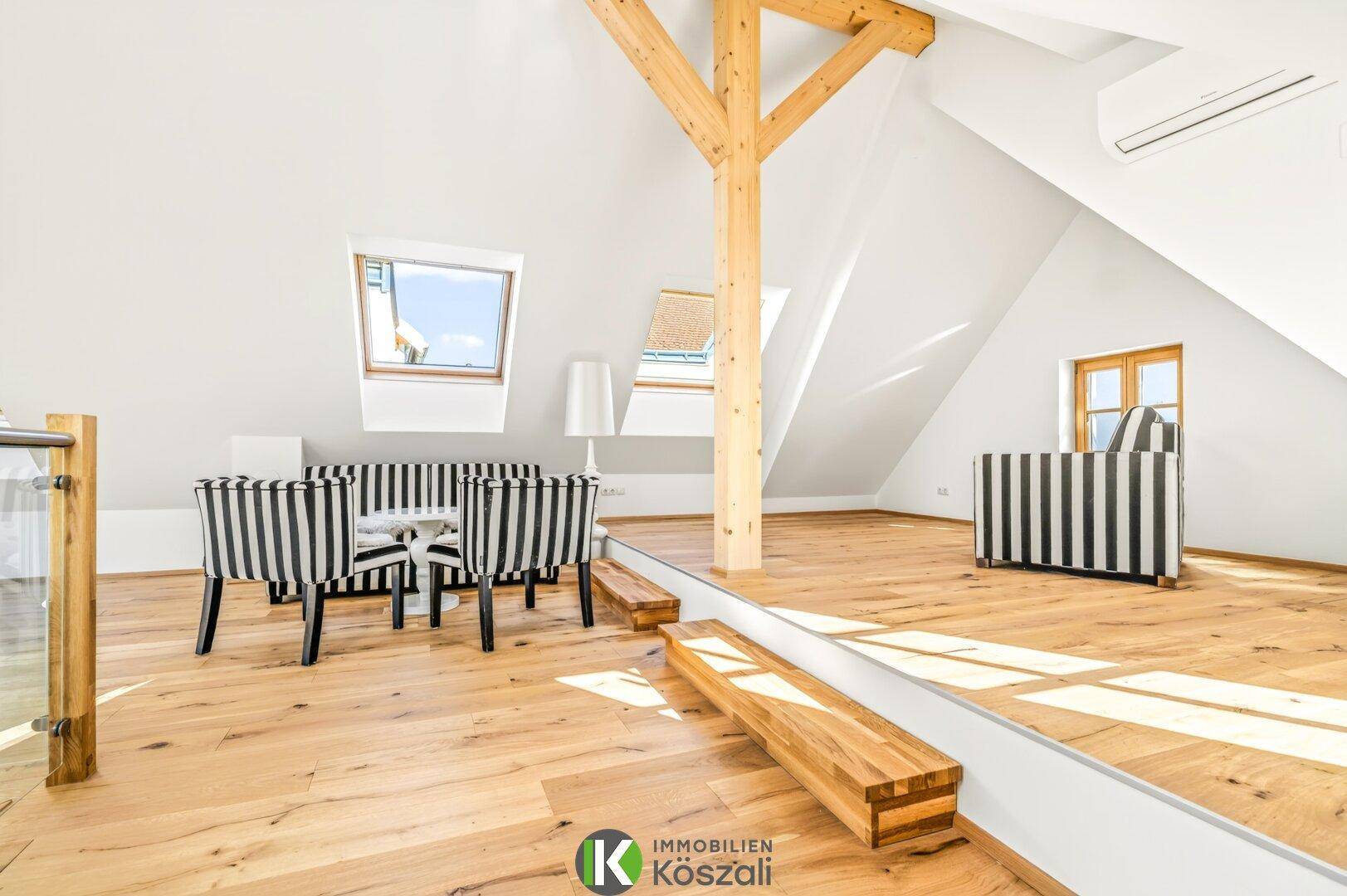 Gemütlicher Dachgeschoss-Wohnbereich mit Holzbalken, Dachfenstern und gestreiften Möbeln.
