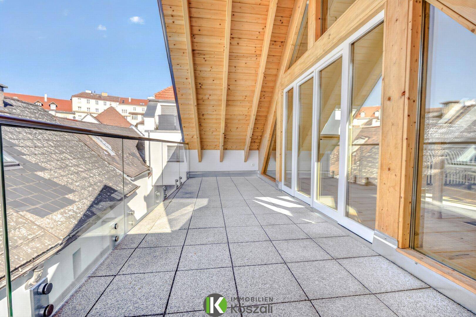 Geräumige Dachterrasse mit modernem Glasgeländer und Panoramablick über die Dächer der Stadt.