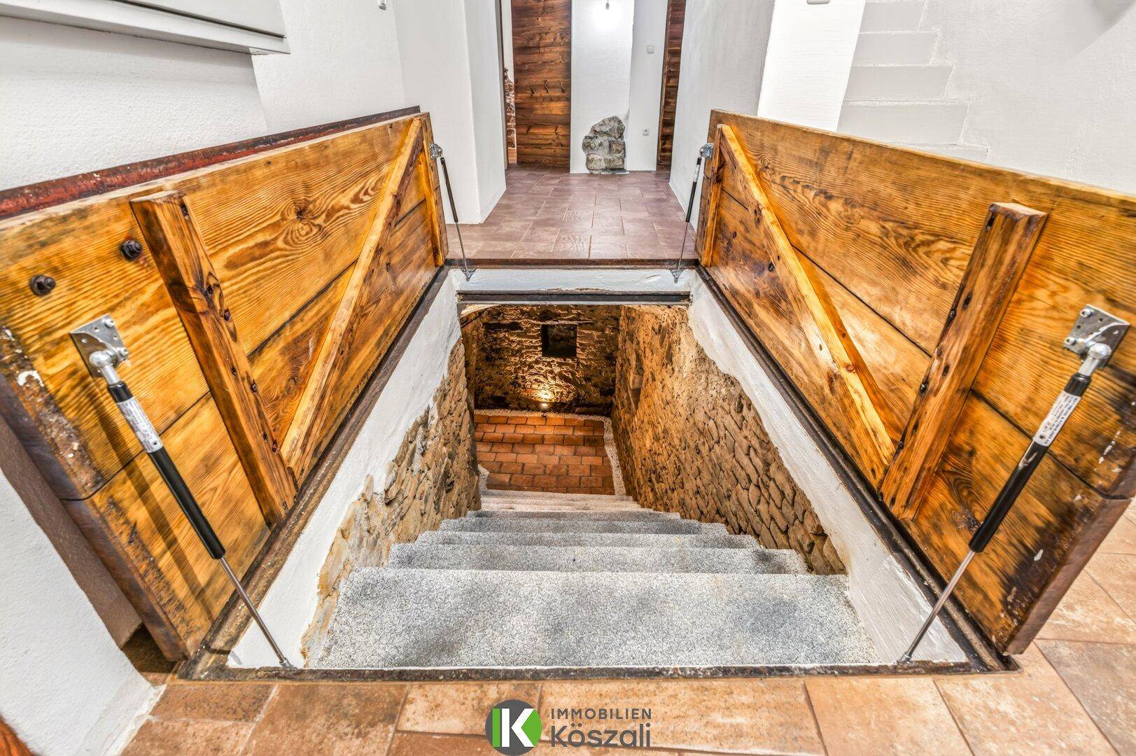 Offener Zugang zum Keller mit Holzluken und Steintreppe, die in den Gewölbekeller führt.