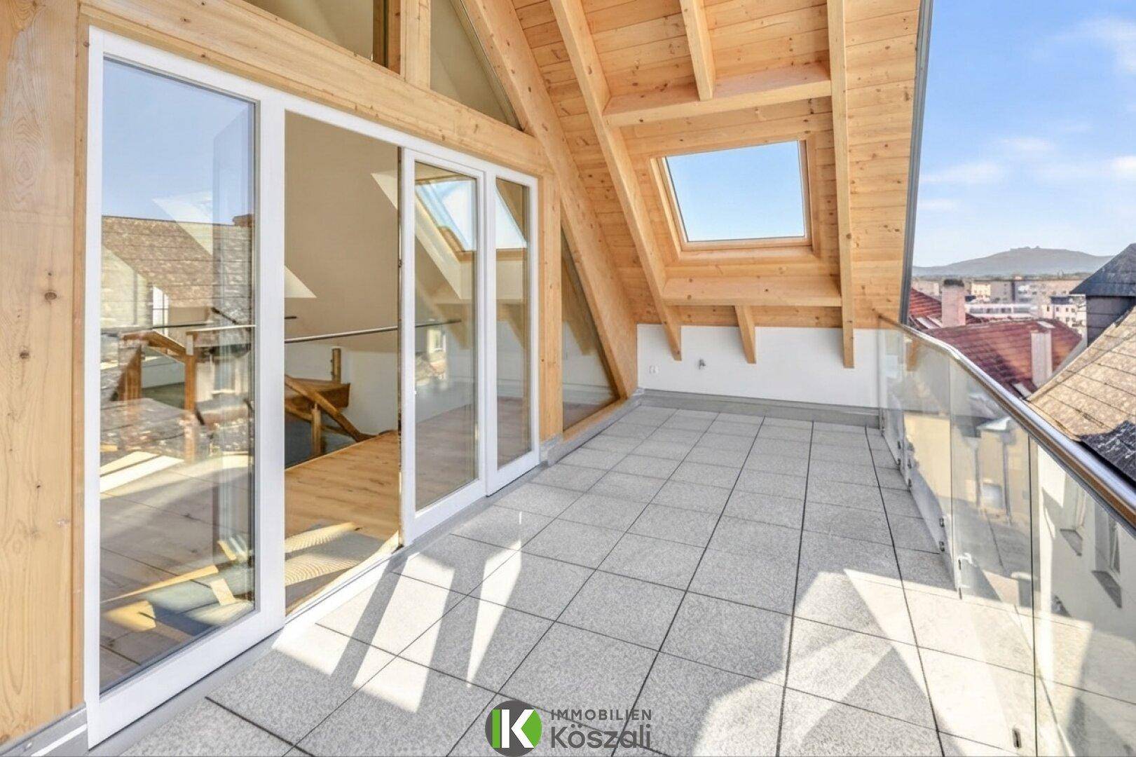 Große Dachterrasse mit Fliesenboden, Glasgeländer und weitem Blick über die Stadt.