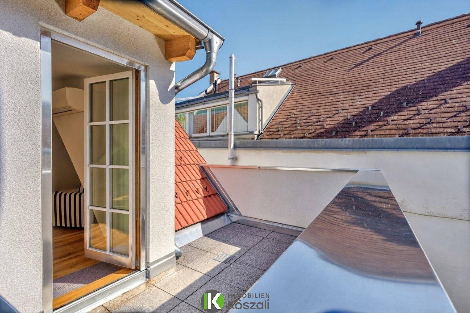 Kleiner Balkon mit Metallgeländer und Blick auf die umliegenden Dächer.