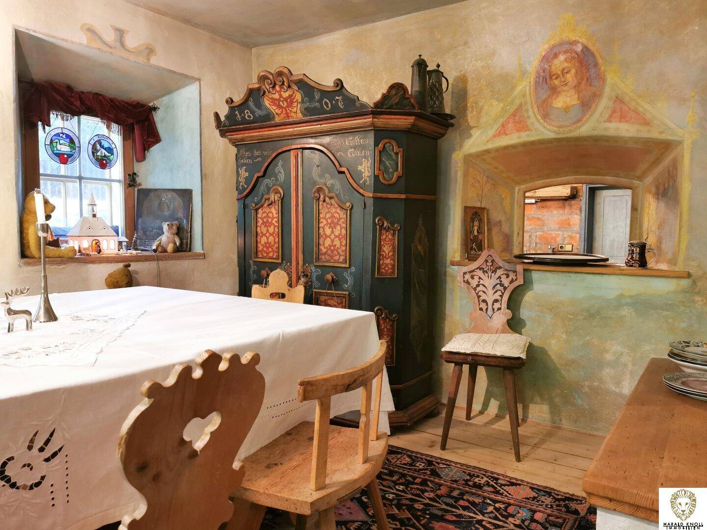 Traditionelles Esszimmer mit bemaltem Schrank, Holzboden und Bleiglasfenstern in rustikalem Ambiente.