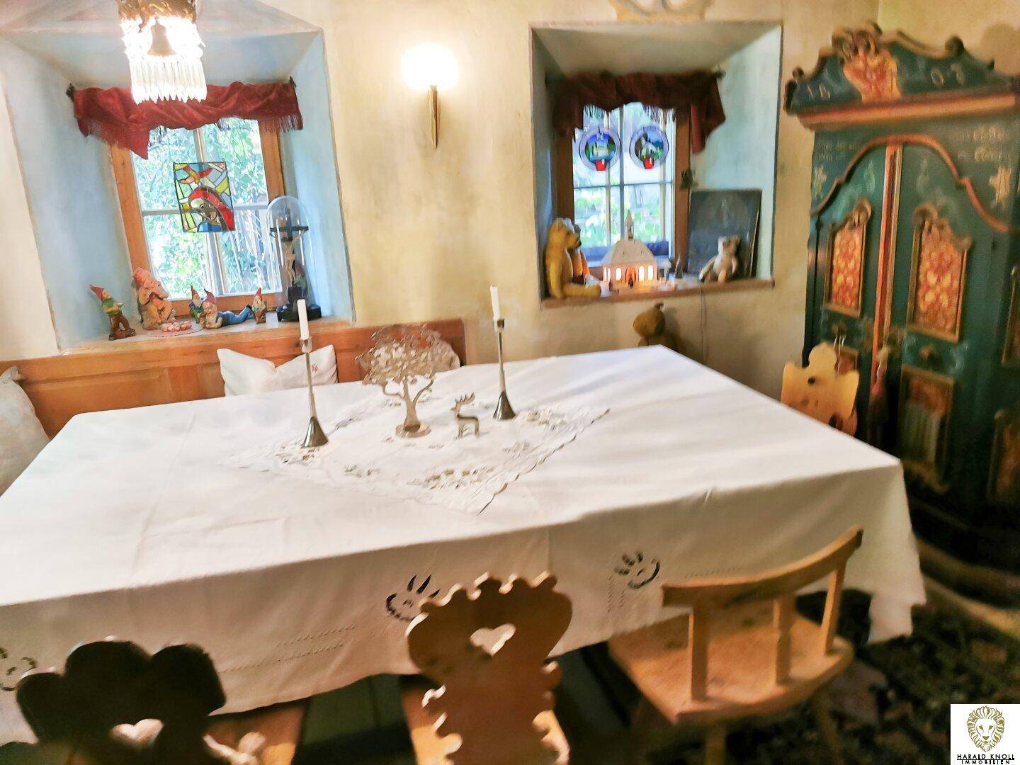 Gemütlicher Essbereich mit großem Holztisch, traditionellen Stühlen und Fenstern mit Vorhängen.