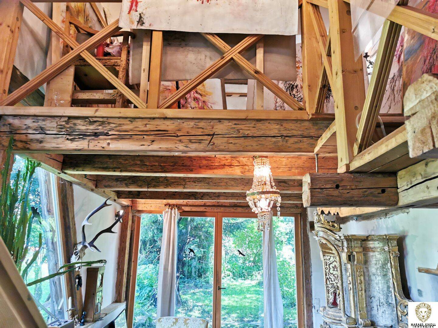 Rustikaler Wohnbereich mit hohen Holzdecken, Kronleuchter und großen Fenstern mit Blick ins Grüne.