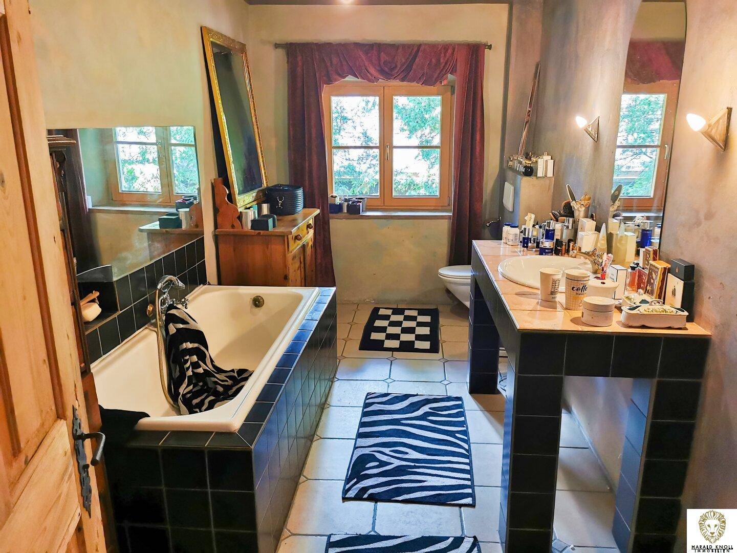 Badezimmer mit Badewanne, Waschtisch, Fliesenboden und Fenster mit Blick ins Grüne.