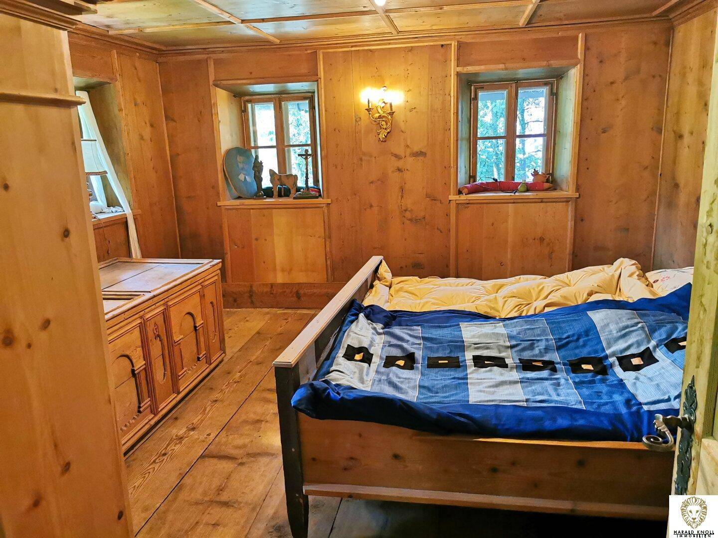 Gemütliches Schlafzimmer mit Holzvertäfelung, Holzbett und traditionellen Möbeln in warmen Tönen.