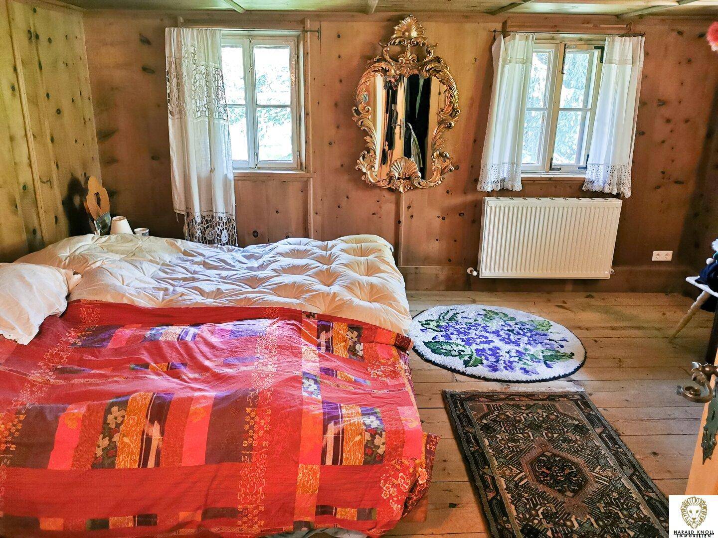 Schlafzimmer mit Holzvertäfelung, Doppelbett, Heizkörper und einem dekorativen goldenen Spiegel.