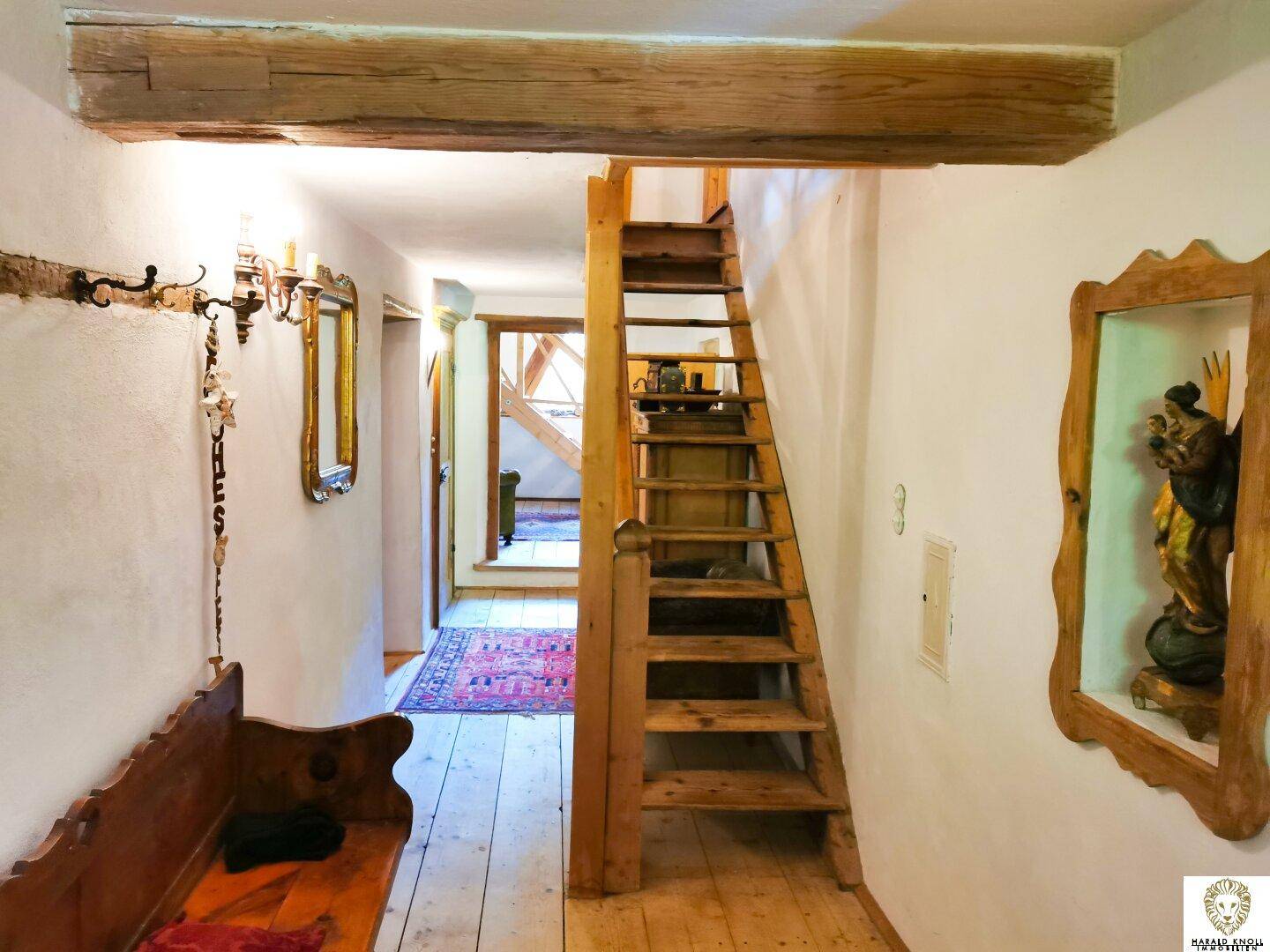 Flur mit Holztreppe, Holzboden, Sitzbank und traditioneller Dekoration an den Wänden.