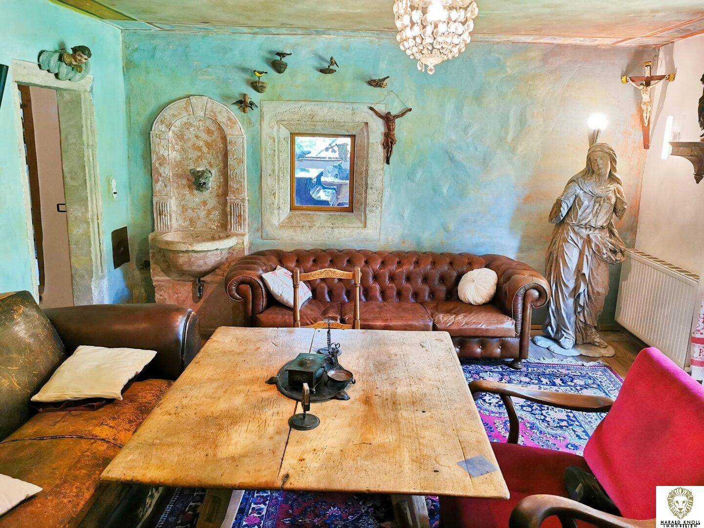 Gemütliches Wohnzimmer mit Chesterfield-Sofa, rustikalen Möbeln und einem dekorativen Wandbrunnen.