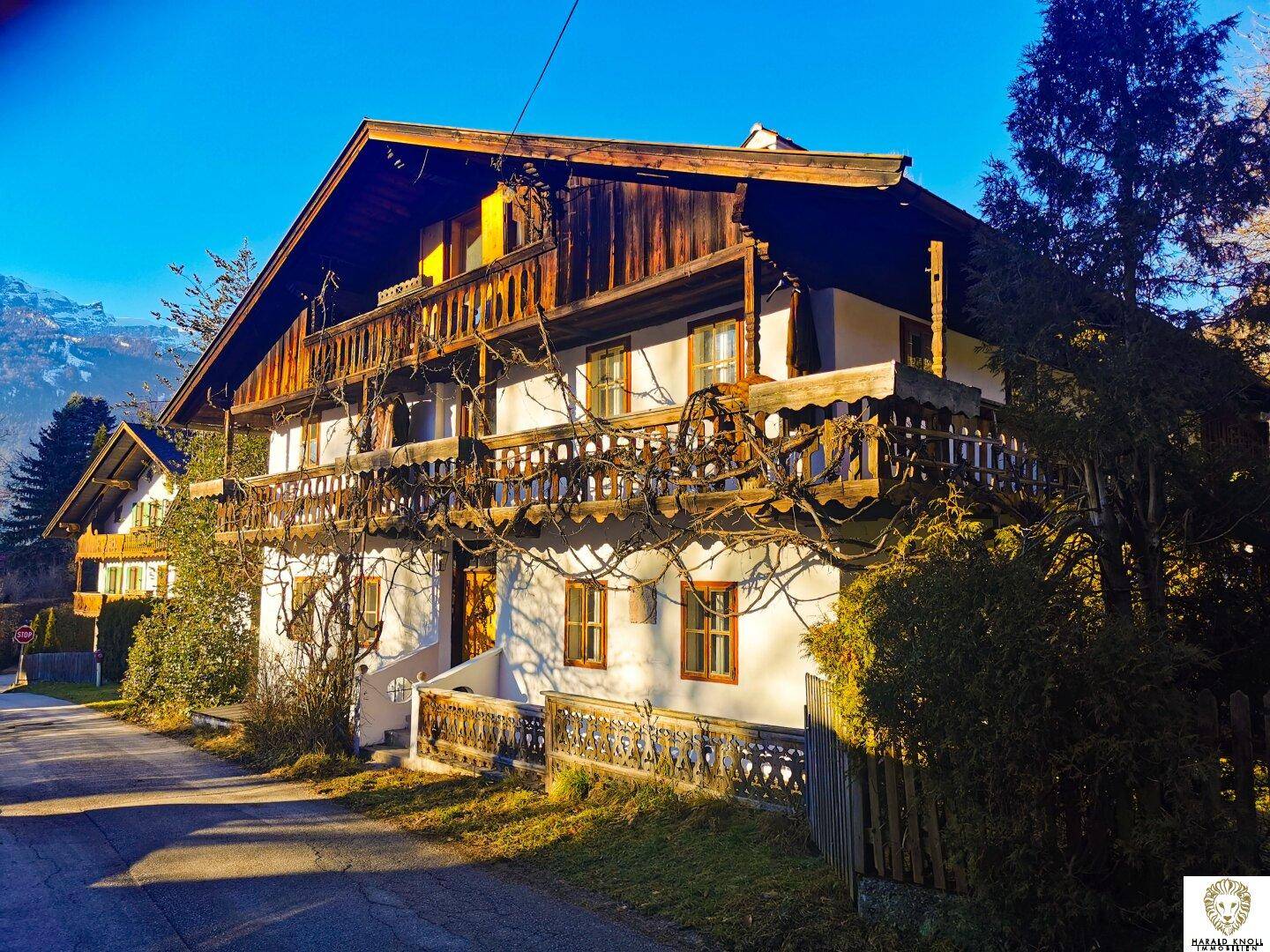 Charmantes alpenländisches Haus mit mehreren Holzbalkonen und traditioneller Fassade an einer Straße.