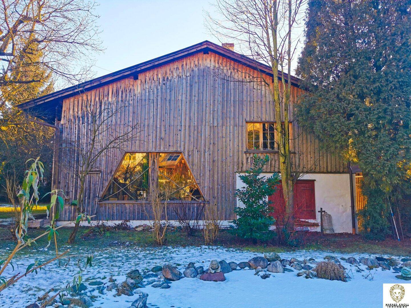 Traditionelles Holzhaus mit großen Fenstern und Gartenbereich im Winter mit leichter Schneedecke.