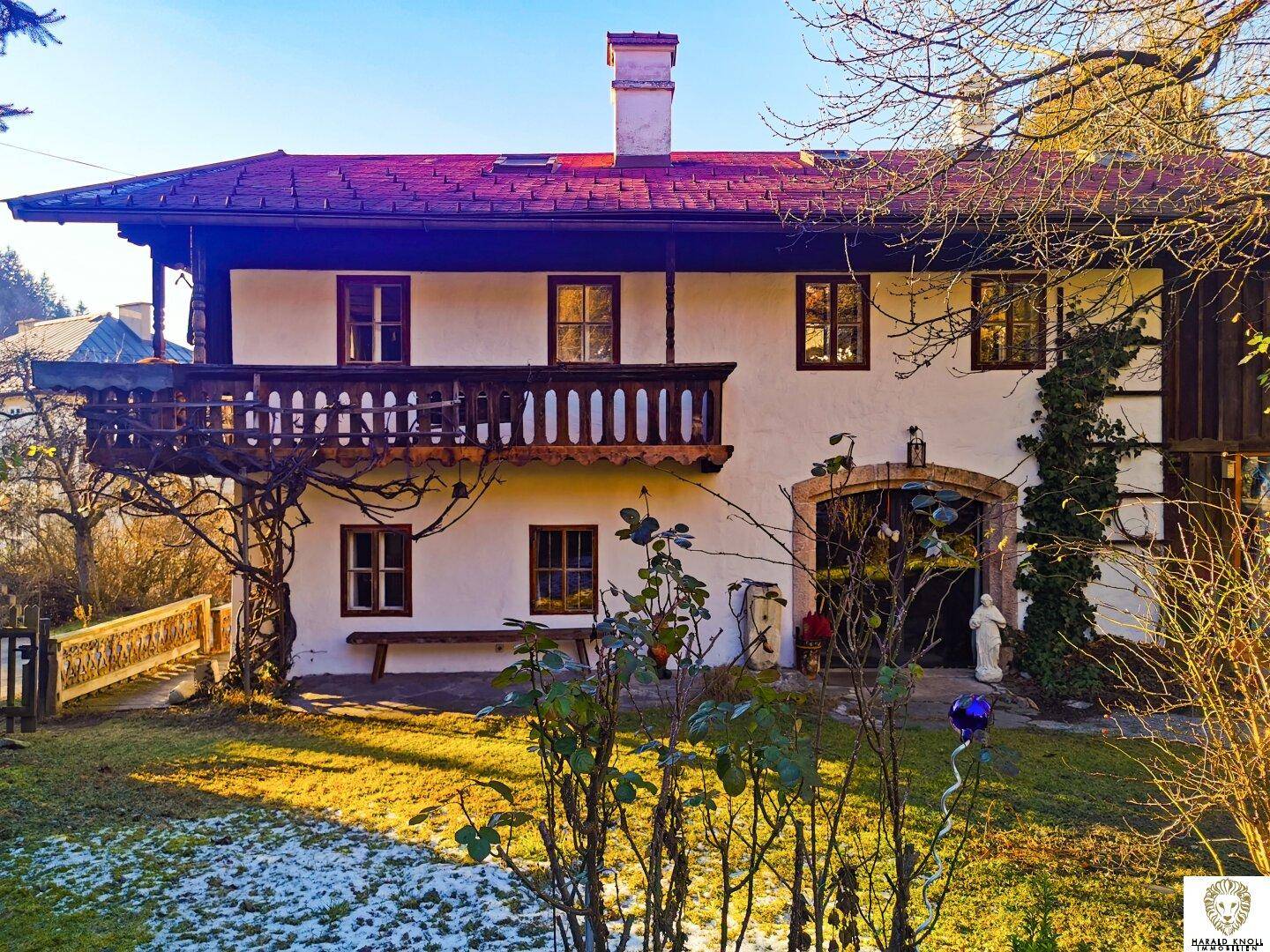 Traditionelles Haus im alpenländischen Stil mit Holzbalkon und Gartenbereich im Sonnenlicht.