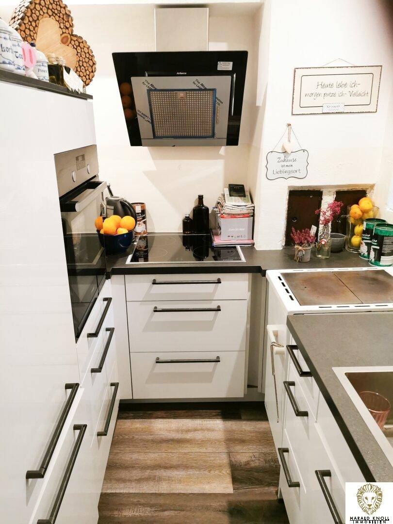 Moderne, kompakte Küche mit weißen Schränken, dunklen Arbeitsplatten und Holzoptik-Boden.