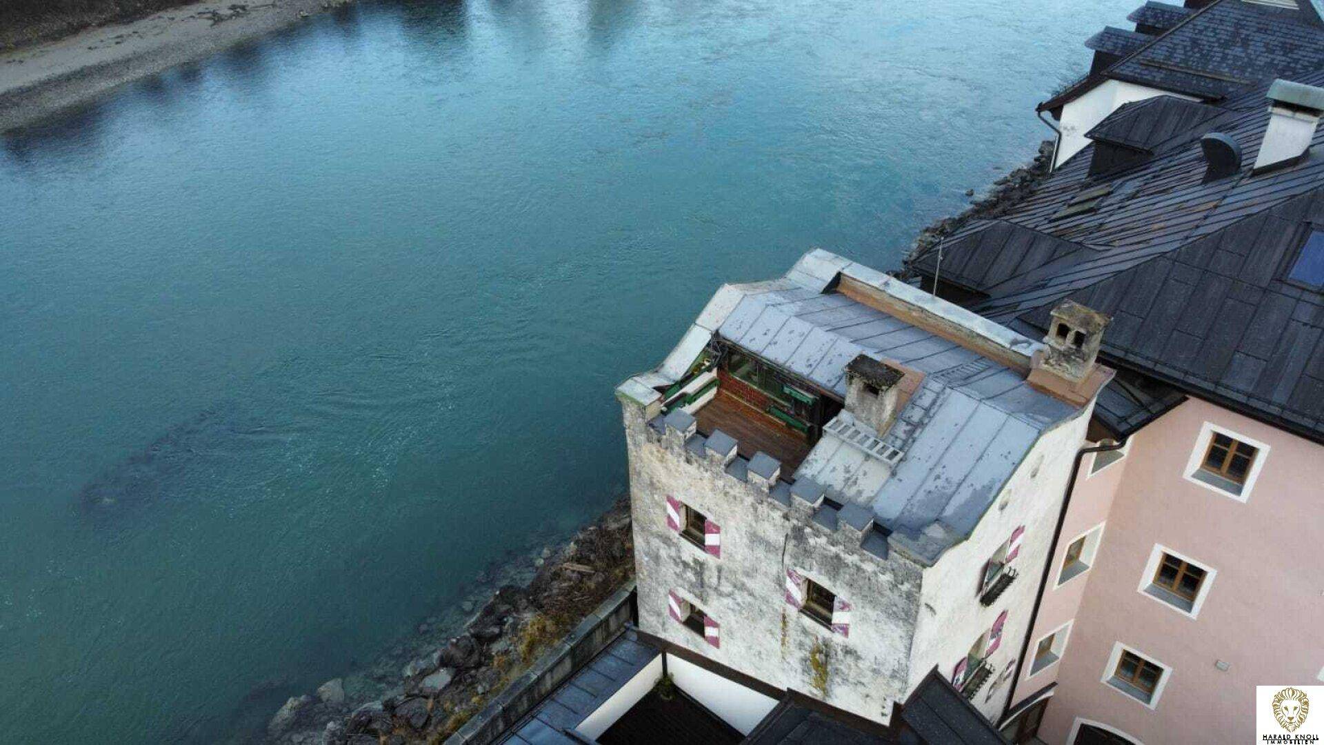 Blick von oben auf ein historisches Gebäude mit Zinnen und einem markanten Dach, direkt am Fluss gelegen.