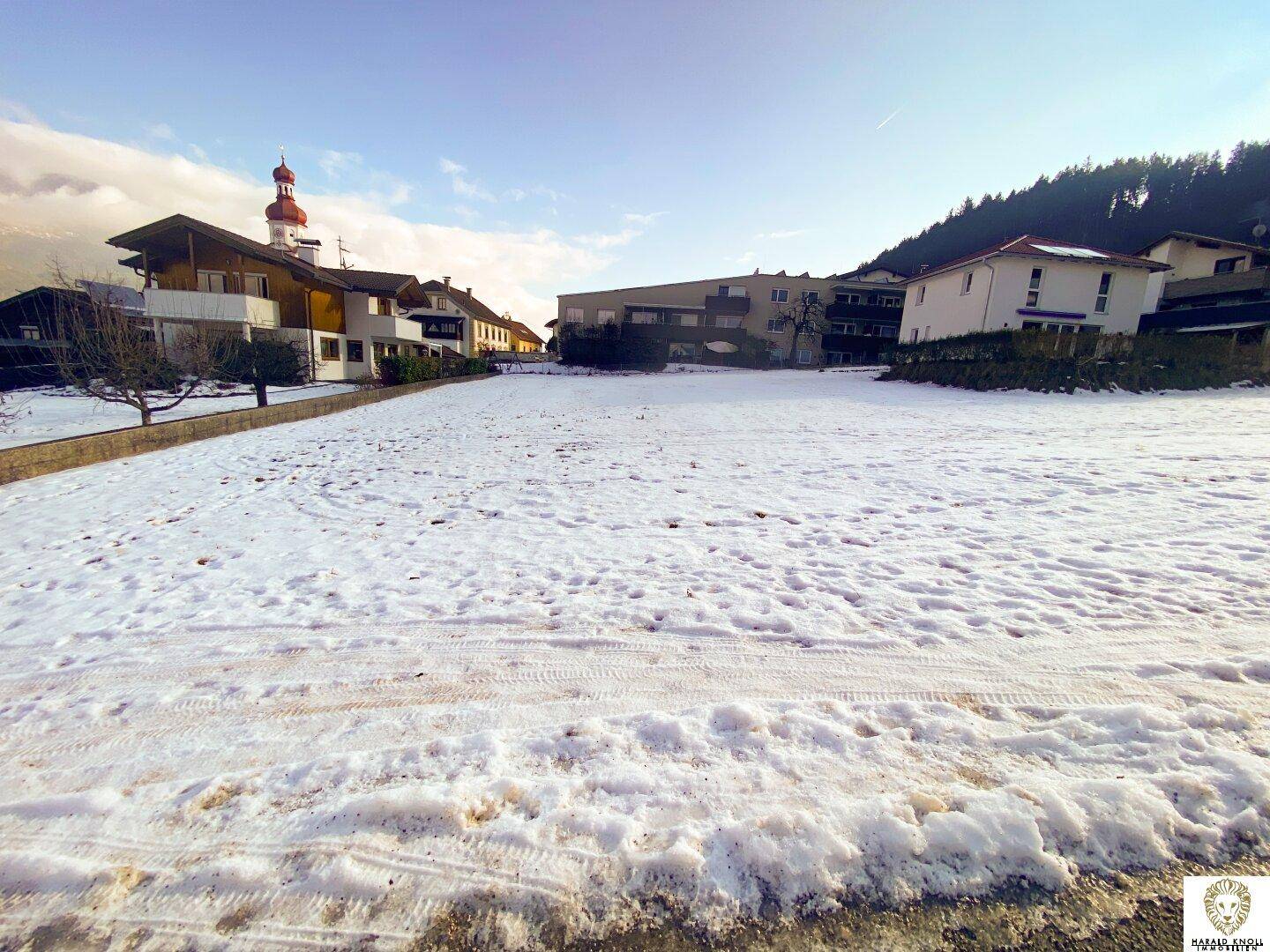 Weitläufiges, schneebedecktes Grundstück in ländlicher Umgebung mit Häusern und einem Kirchturm.