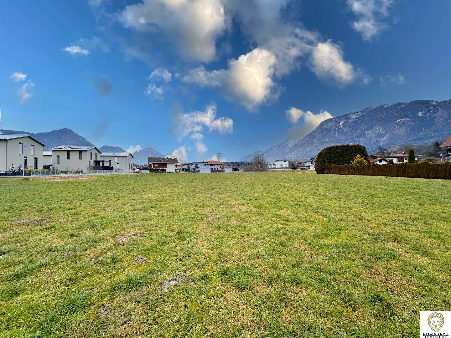 Weitläufige grüne Fläche mit Panoramablick auf die umliegende Berglandschaft und Wohngebäude.