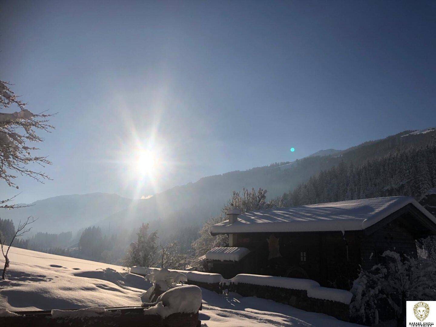 Idyllisches Holzhaus in einer tief verschneiten Berglandschaft unter blauem Himmel.