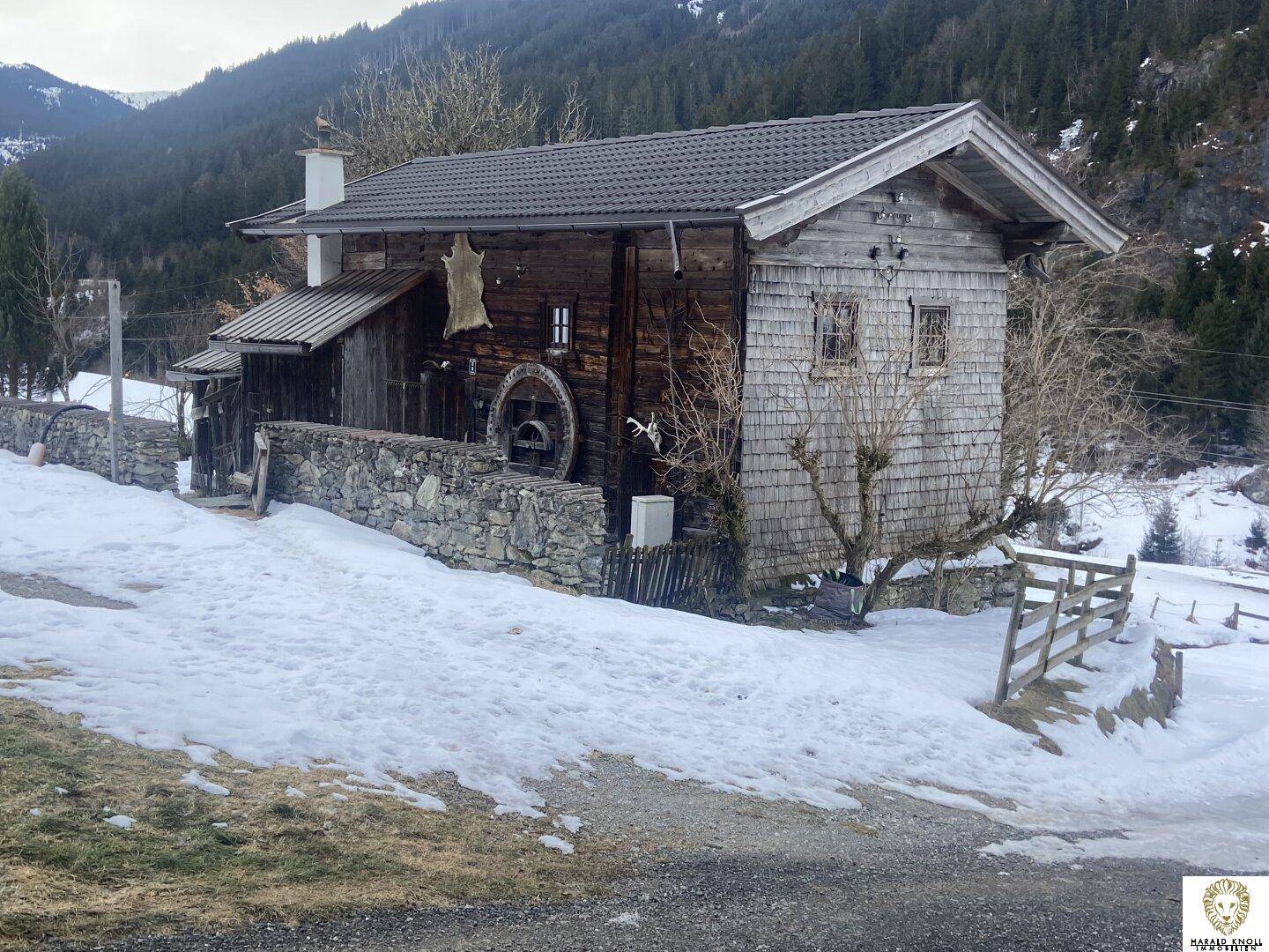 Traditionelles Holzhaus mit Steinfundament und verschneiter Umgebung in den Alpen.
