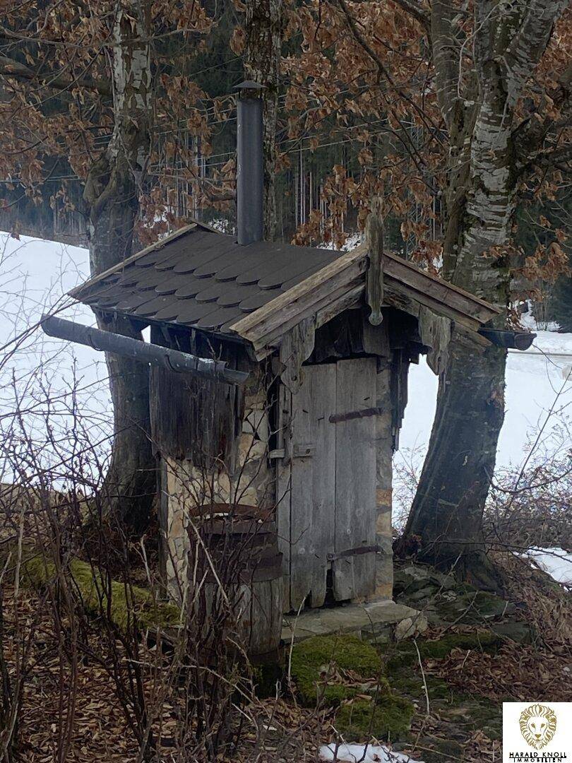 Kleines, rustikales Holz- und Steinhäuschen mit Schornstein in winterlicher Umgebung.