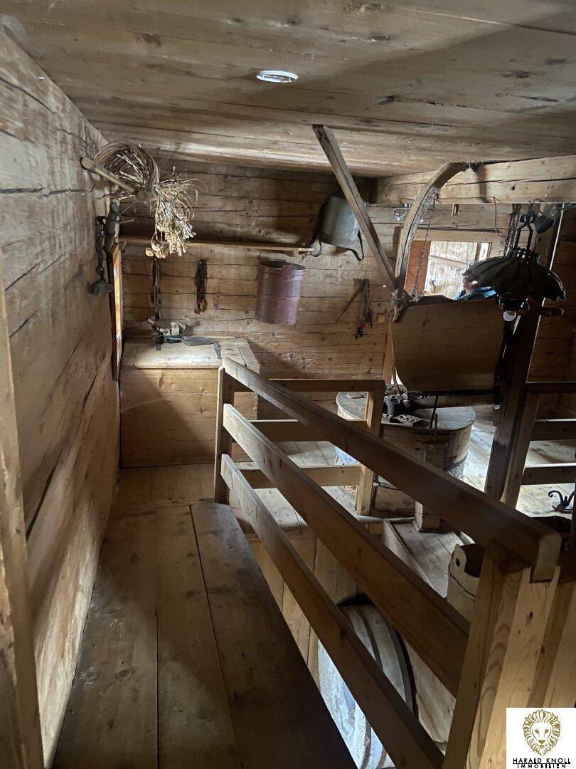 Innenansicht einer historischen Mühle mit Holzbalken, rustikalen Geräten und einer Holzbrüstung, die den Raum strukturiert.