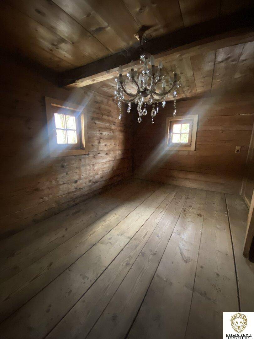 Leerer Raum mit Holzwänden, Holzboden und einem eleganten Kronleuchter, der für eine besondere Atmosphäre sorgt.