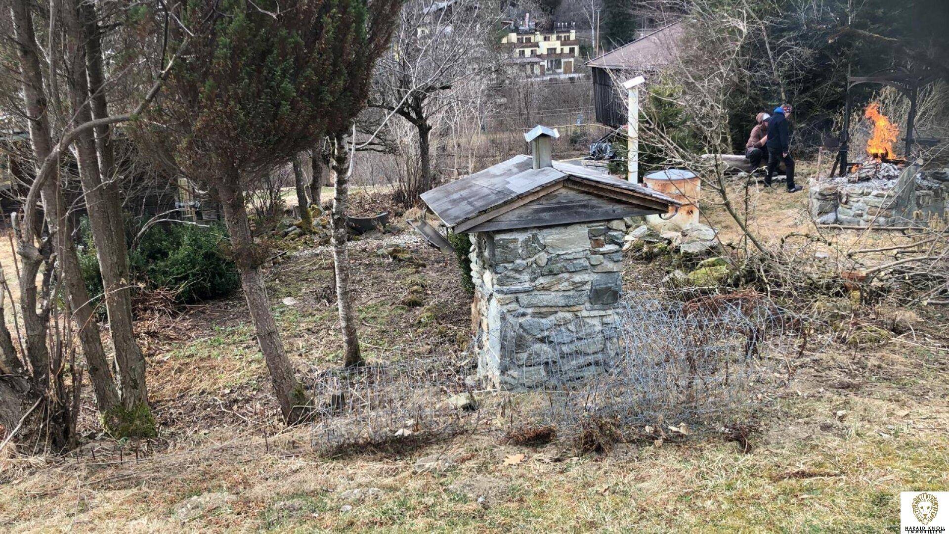 Gartenbereich mit einem Steinhäuschen und einem Feuerplatz im Hintergrund.