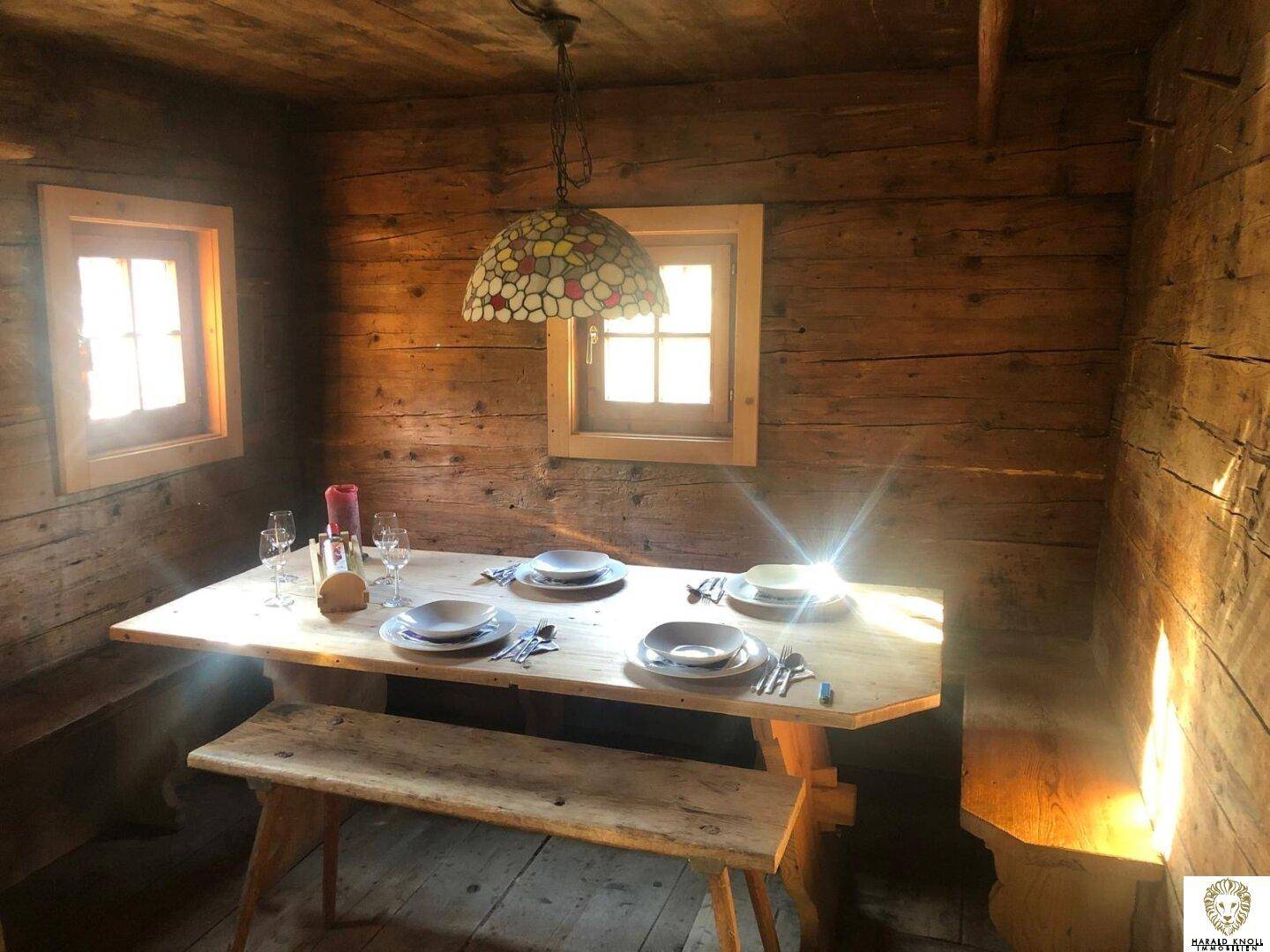 Gemütlicher Essbereich mit Holztisch und Bänken, beleuchtet von einer bunten Lampe.