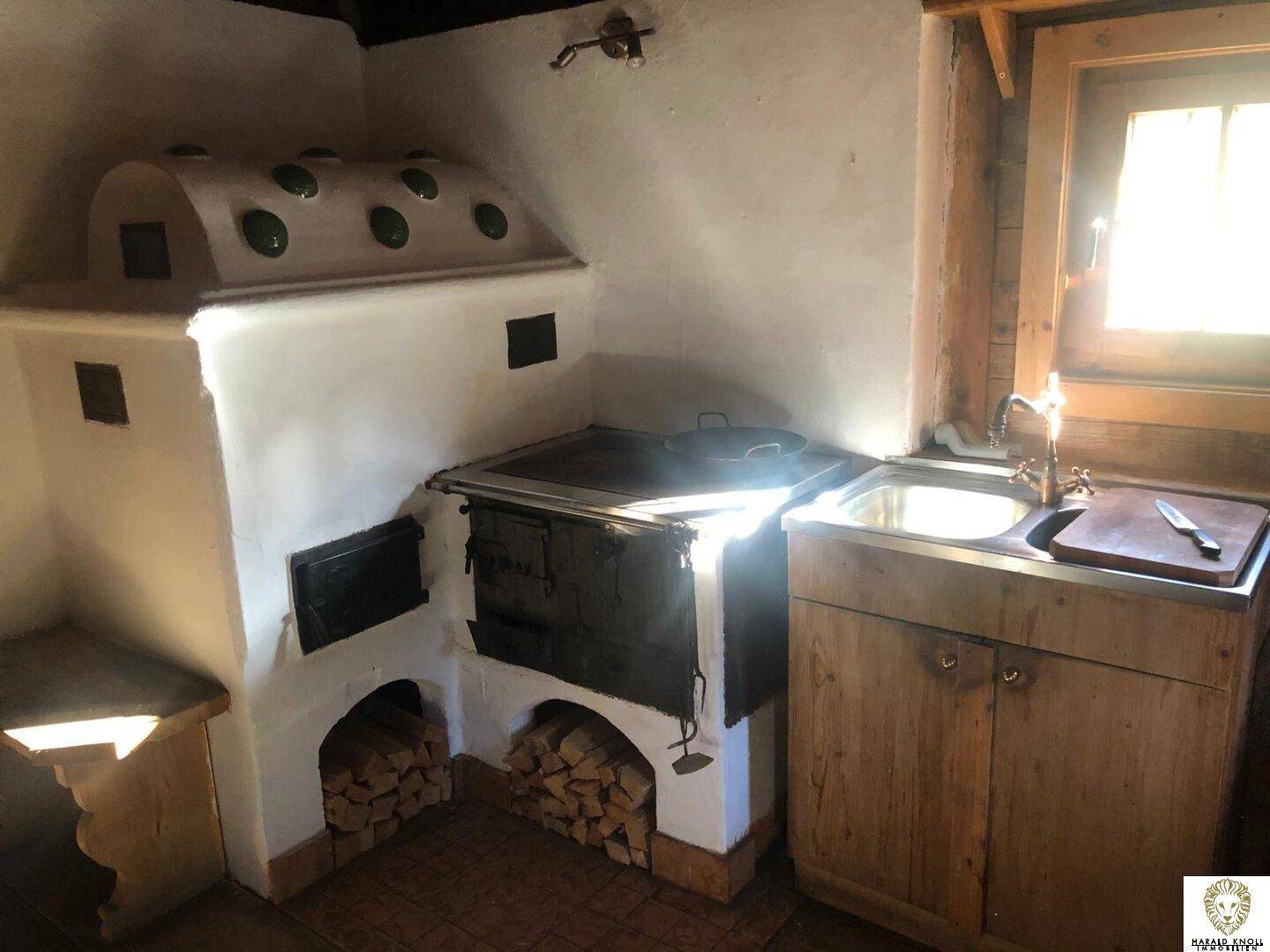 Traditionelle Küche mit Kachelofen, Holzherd und Spülbecken in rustikalem Ambiente.