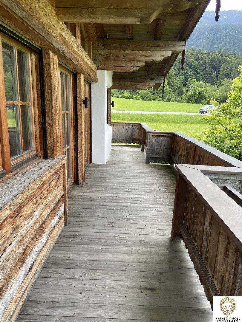 Langer Holzbalkon mit rustikalem Geländer und Blick auf die grüne Landschaft.