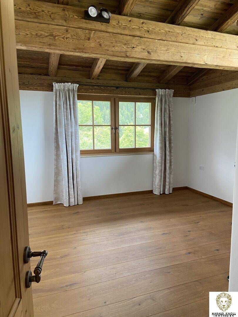 Helles Schlafzimmer mit Holzbalkendecke, Holzboden und Fenster mit Blick ins Grüne.