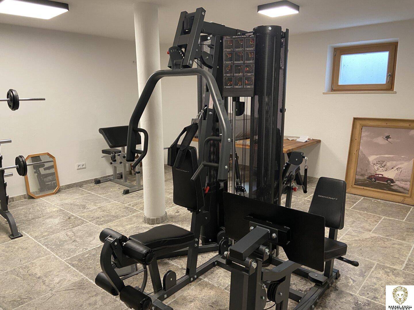 Fitnessraum im Untergeschoss mit verschiedenen Trainingsgeräten und Steinfliesenboden.