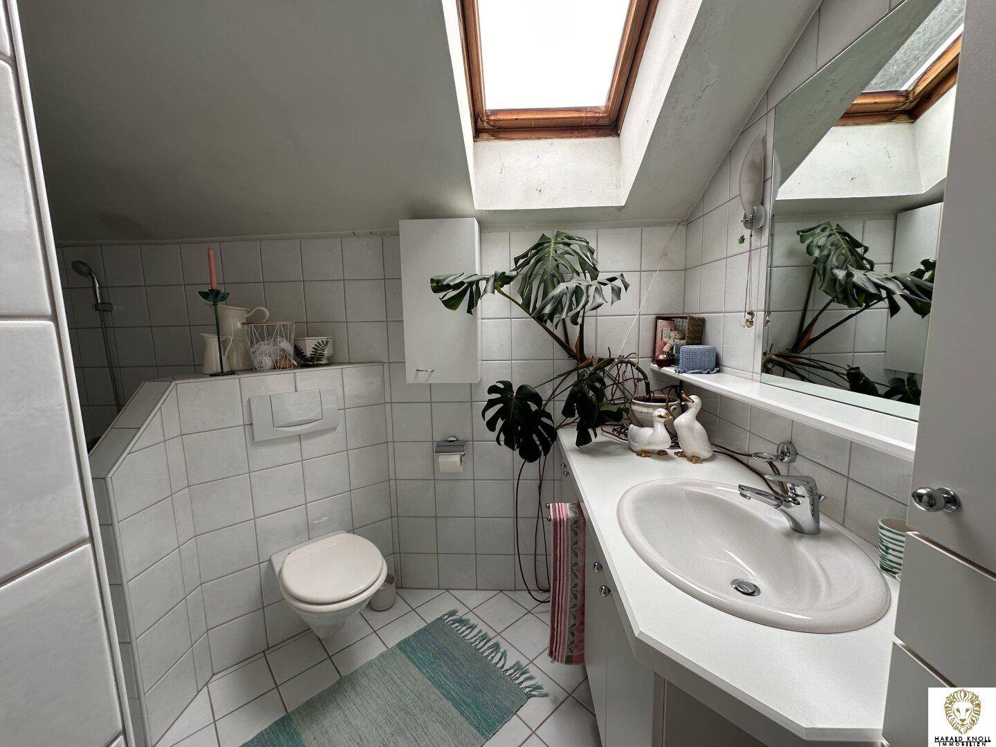 Helles Badezimmer mit Dachfenster, weißen Fliesen, Waschbecken und WC, gut beleuchtet.