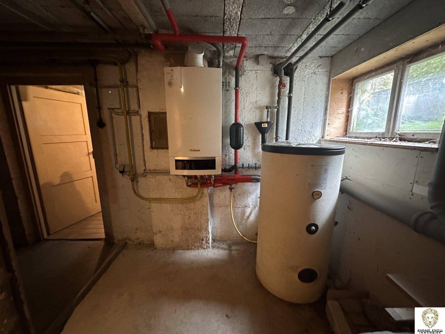 Kellerraum mit Heizungsanlage, Warmwasserspeicher und sichtbaren Rohren, funktionaler Bereich.