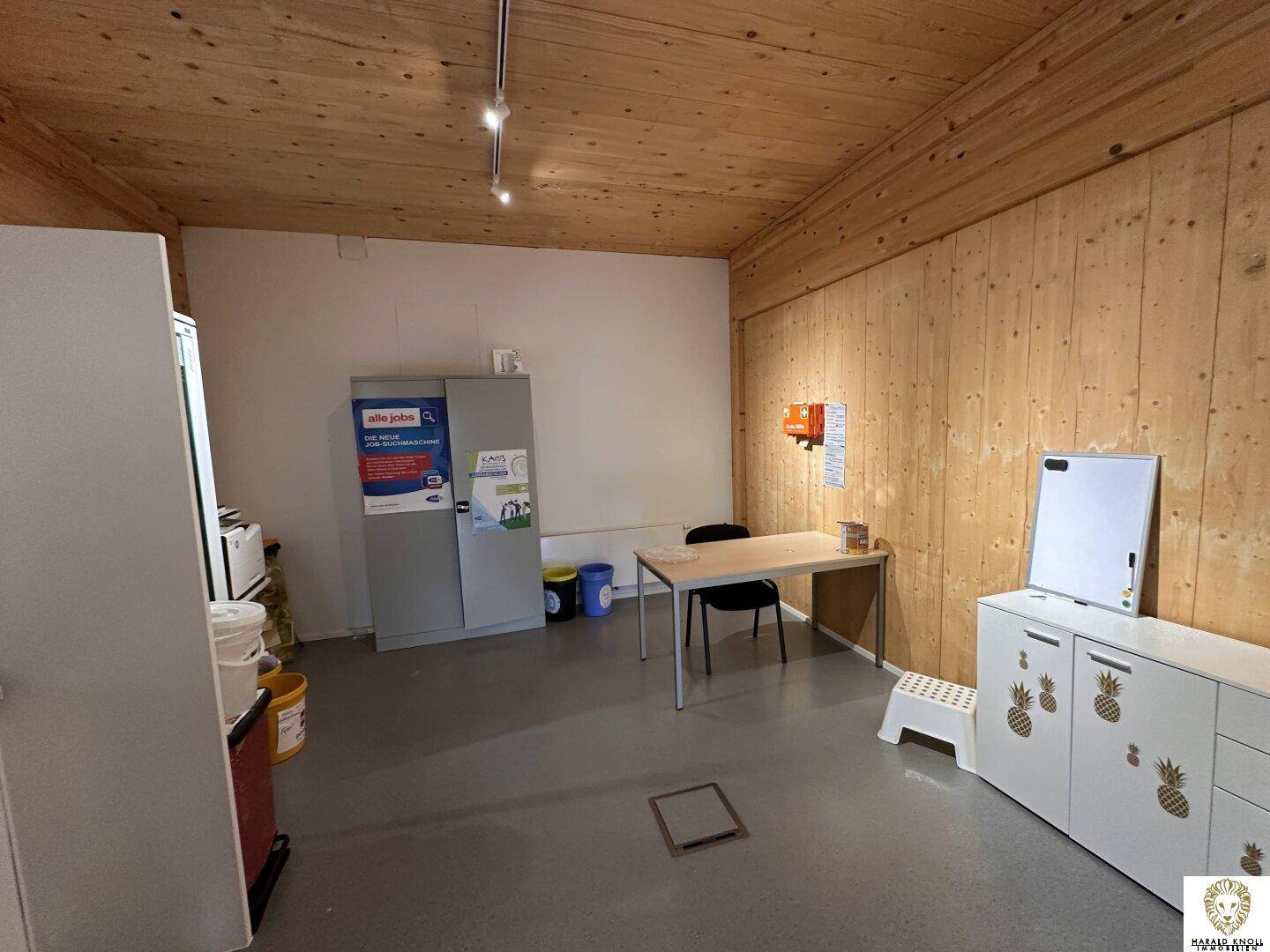 Einfacher Büroraum mit Schrank, Schreibtisch und Whiteboard, funktional eingerichtet.