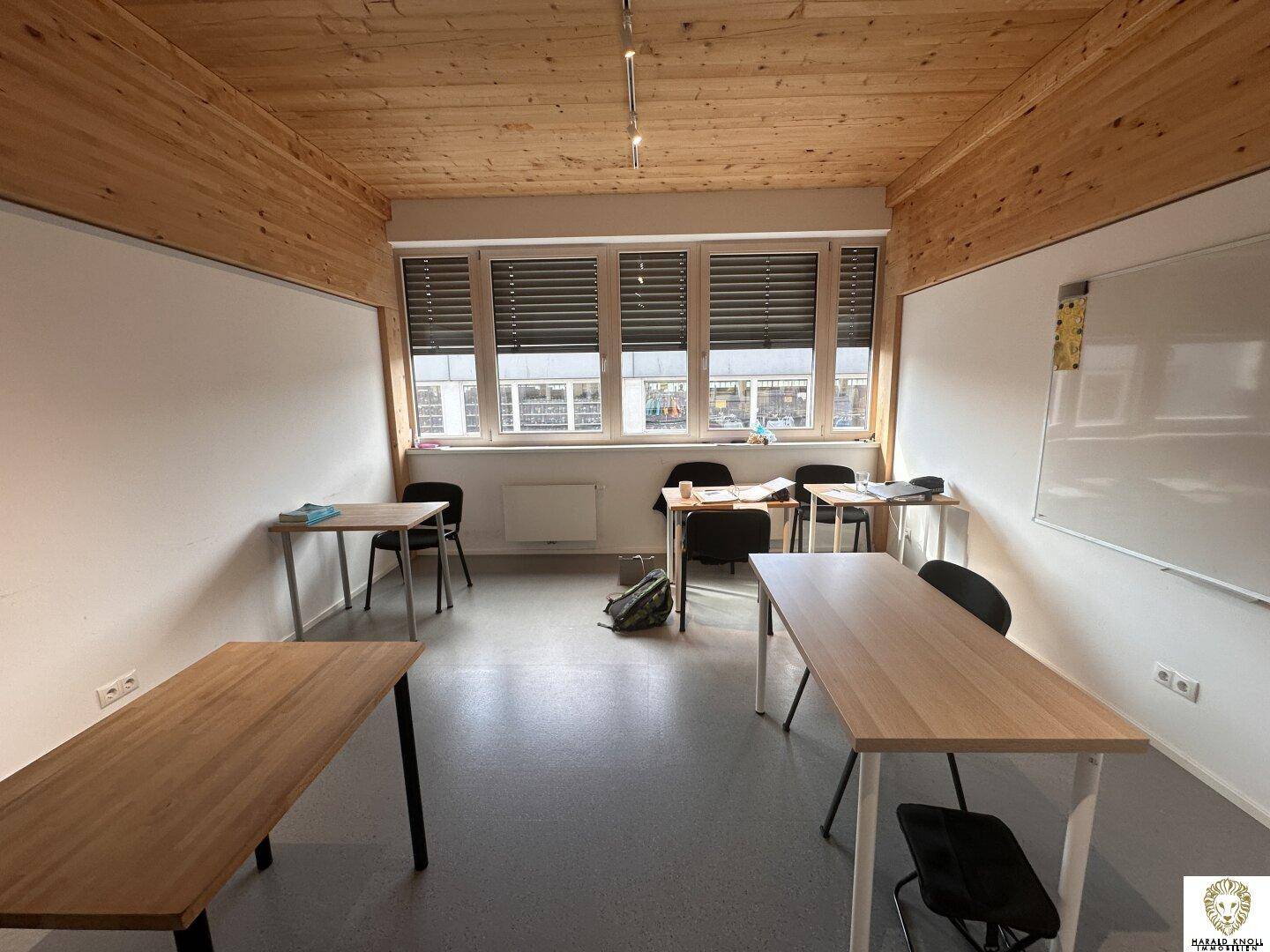 Heller Schulungsraum mit mehreren Tischen und Stühlen, großen Fenstern und Whiteboard.