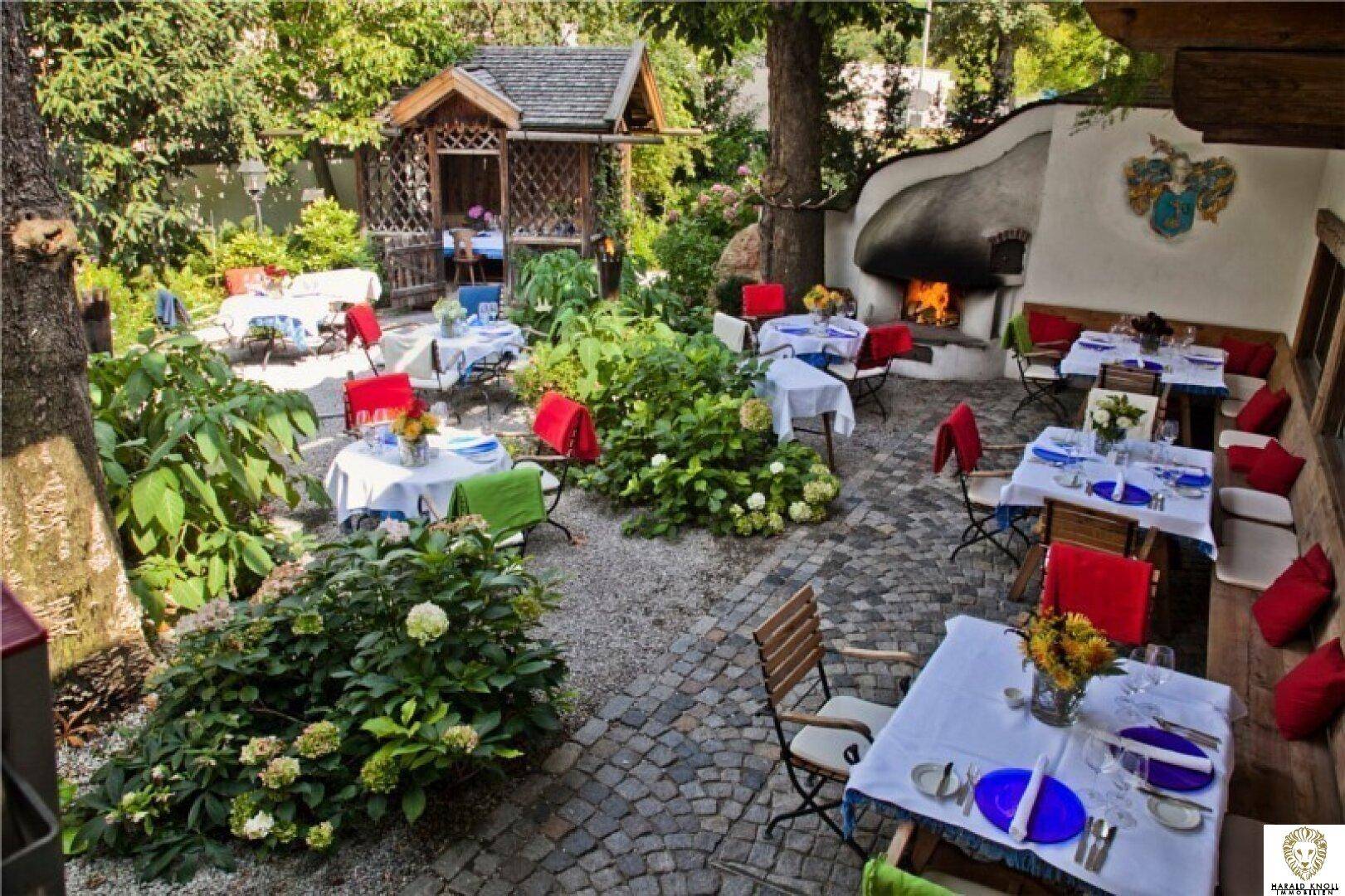 Malerischer Biergarten mit Kopfsteinpflaster, üppiger Bepflanzung und einem Außenkamin.