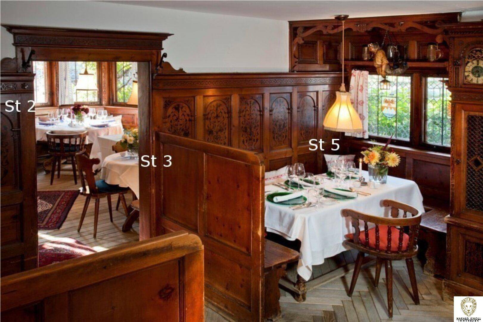 Gemütlicher Essbereich mit traditionellen Holzvertäfelungen und Blick ins Grüne durch die Fenster.
