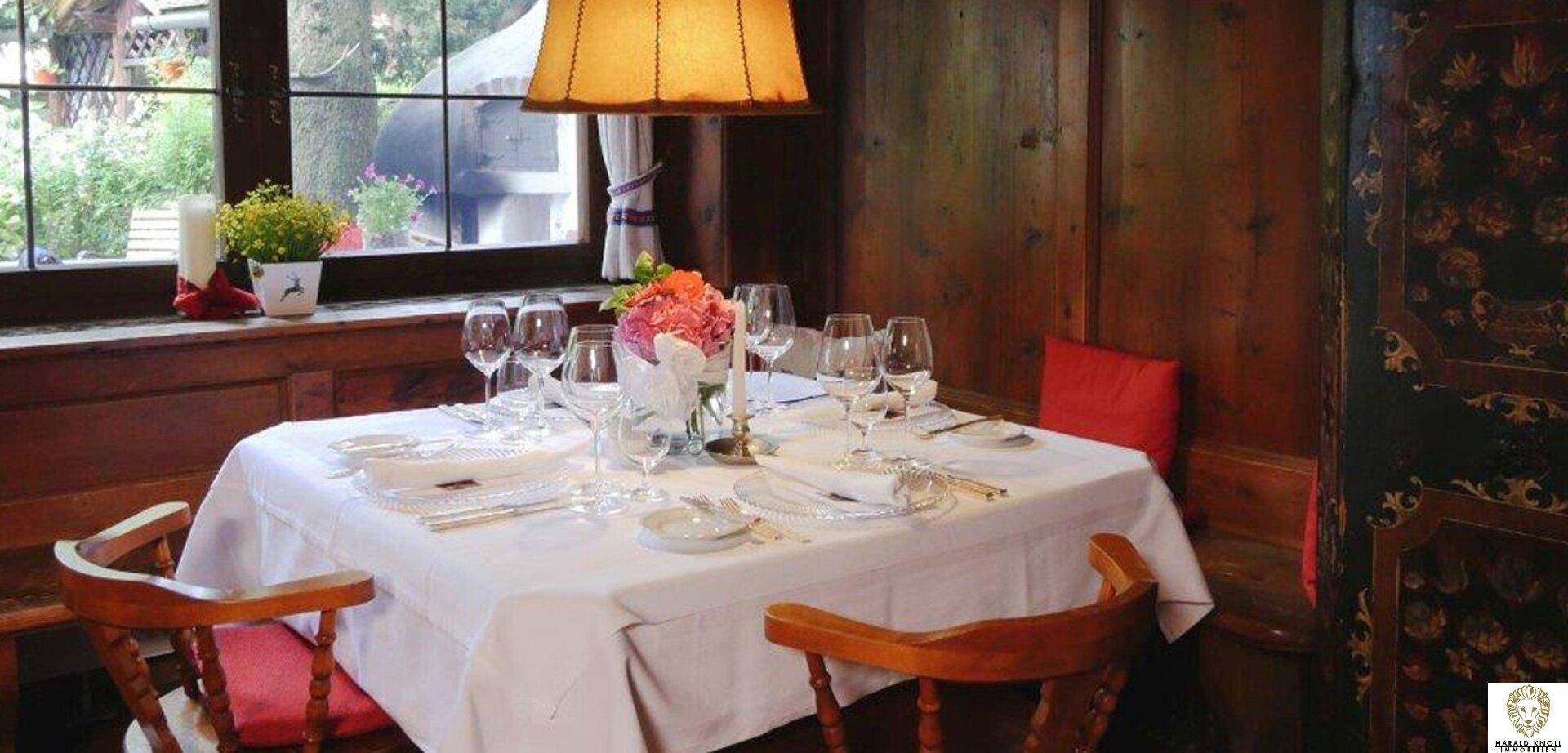 Gemütlicher Essbereich mit gedecktem Tisch, Blumenarrangement und Blick ins Grüne durch das Fenster.