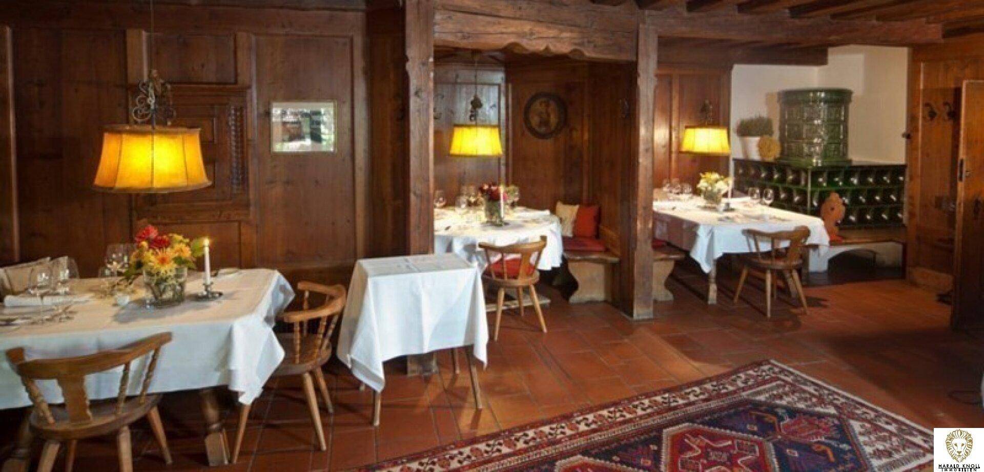 Mehrere Essbereiche in einem traditionellen Restaurant mit Holzeinrichtung, Teppichen und Kachelofen.