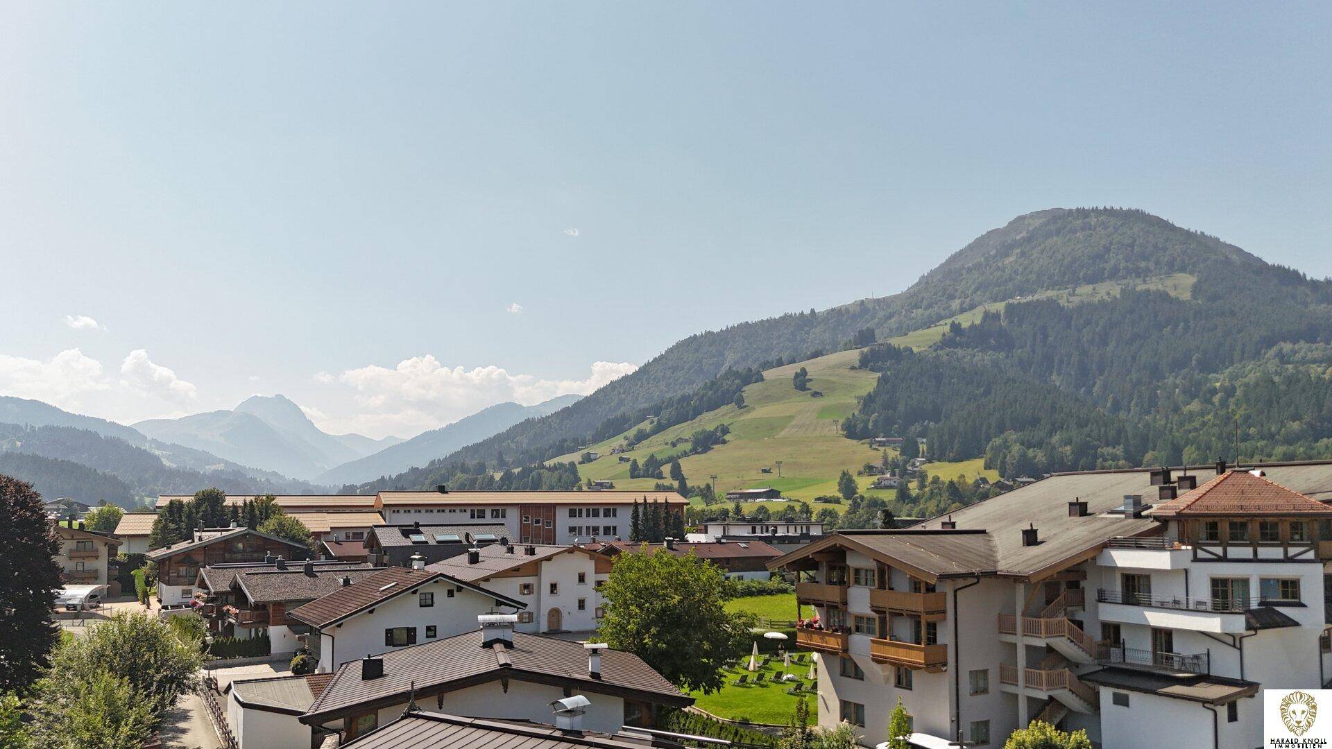 Malerischer Blick auf ein Dorf mit traditionellen Häusern und einer beeindruckenden grünen Berglandschaft.