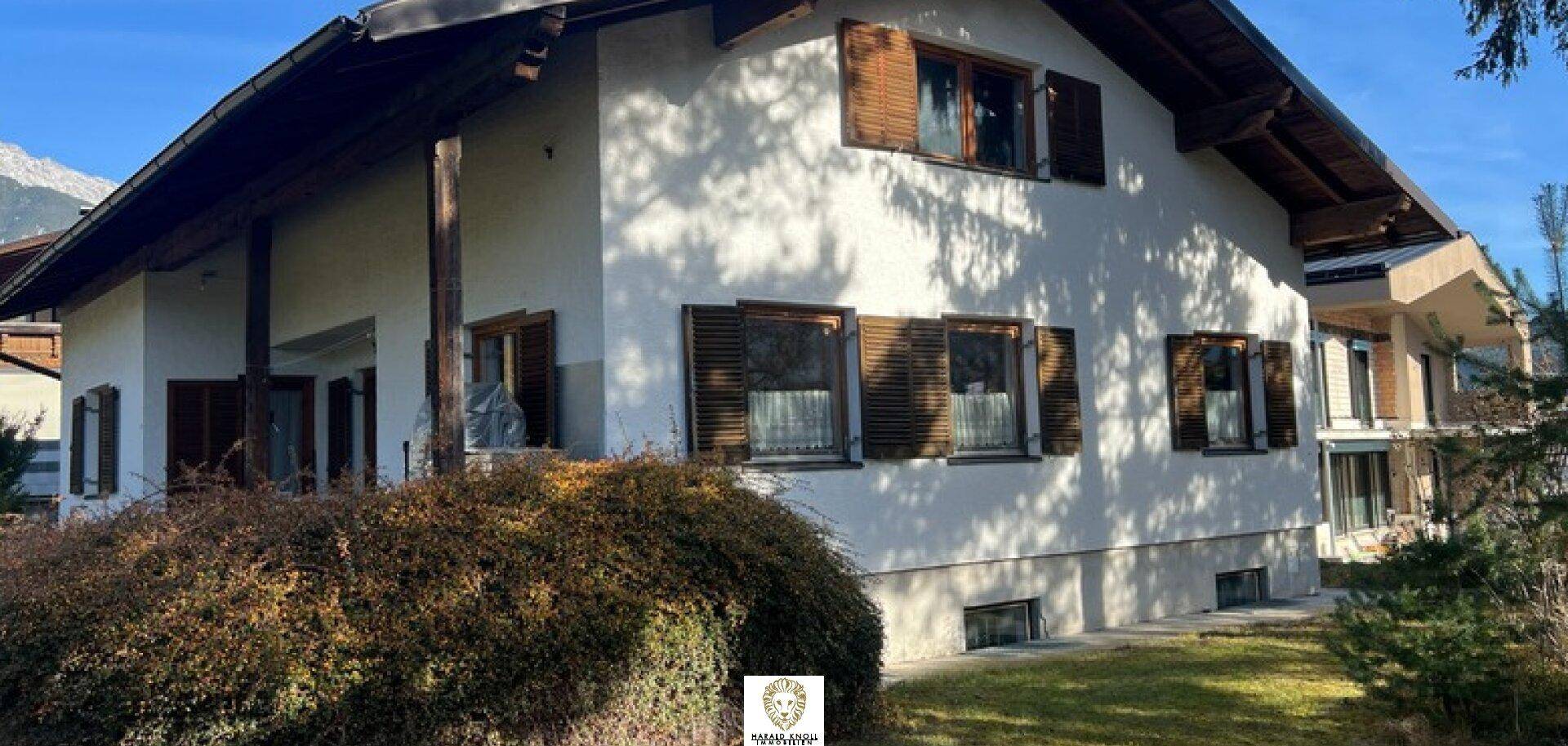 Ansicht der Hausfassade mit weißen Wänden, traditionellen Holzfensterläden und gepflegten Büschen.