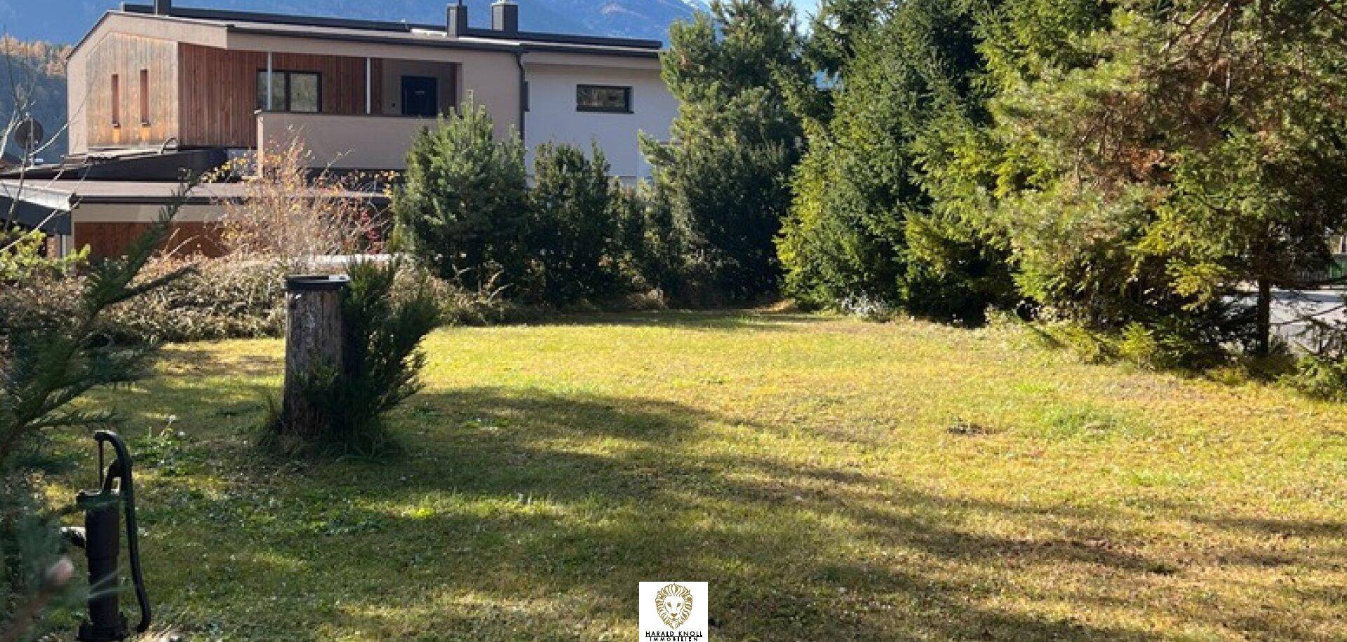 Weitläufige Rasenfläche mit Bäumen und Blick auf die umliegende Bebauung und Bergkulisse.