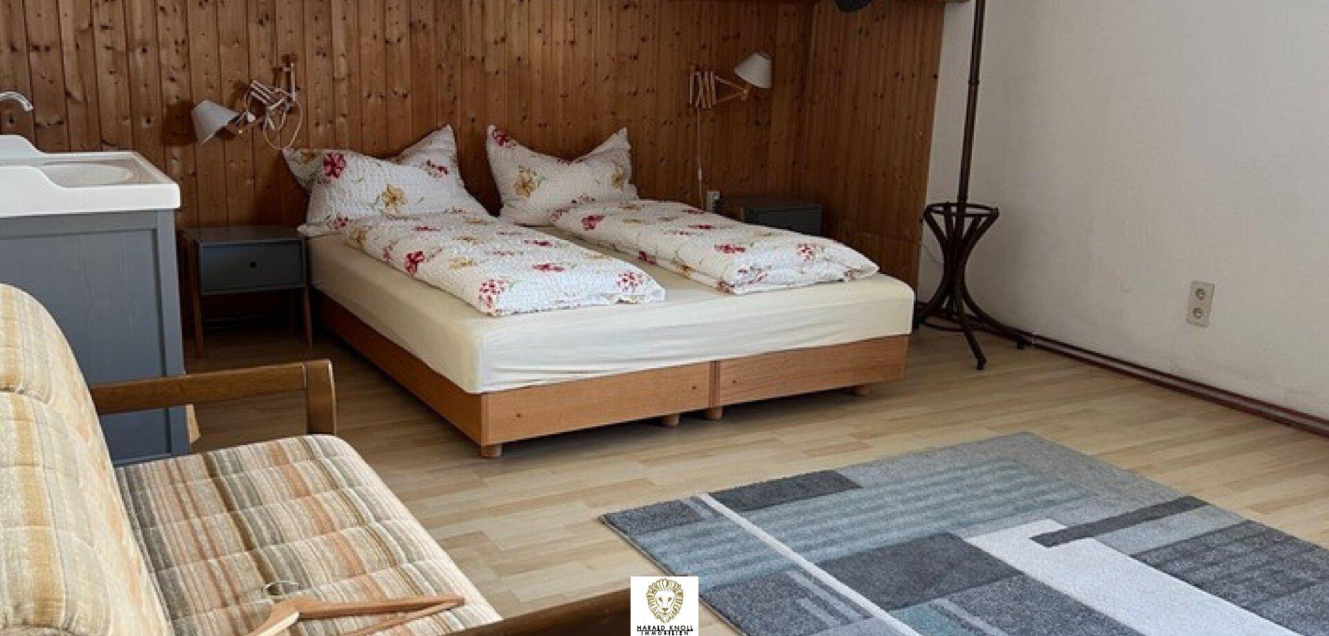 Rustikales Schlafzimmer mit Holzwänden, zwei Einzelbetten und einem bequemen Sofa.