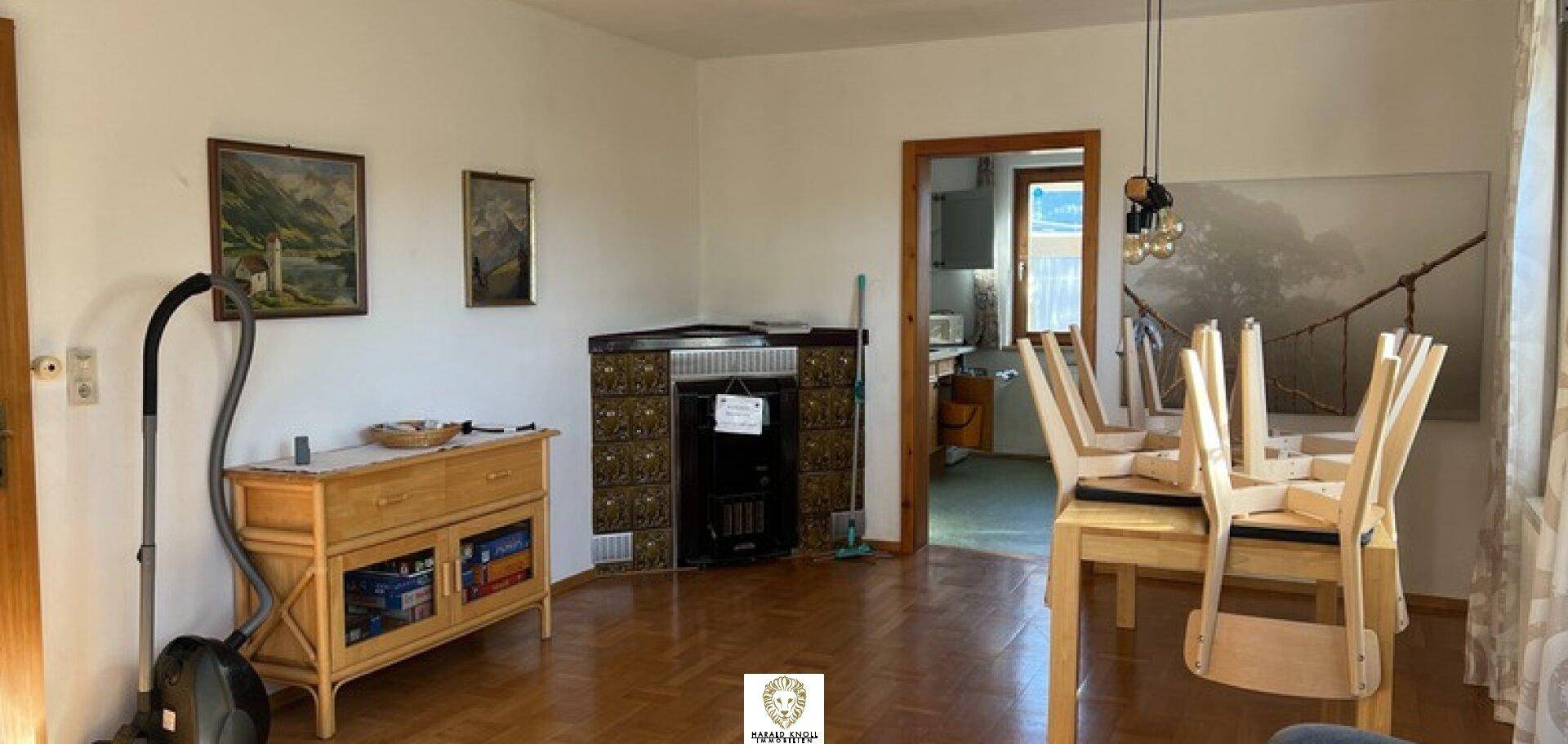 Gemütlicher Wohn-Essbereich mit traditionellem Kachelofen und Holzboden, angrenzend an die Küche.